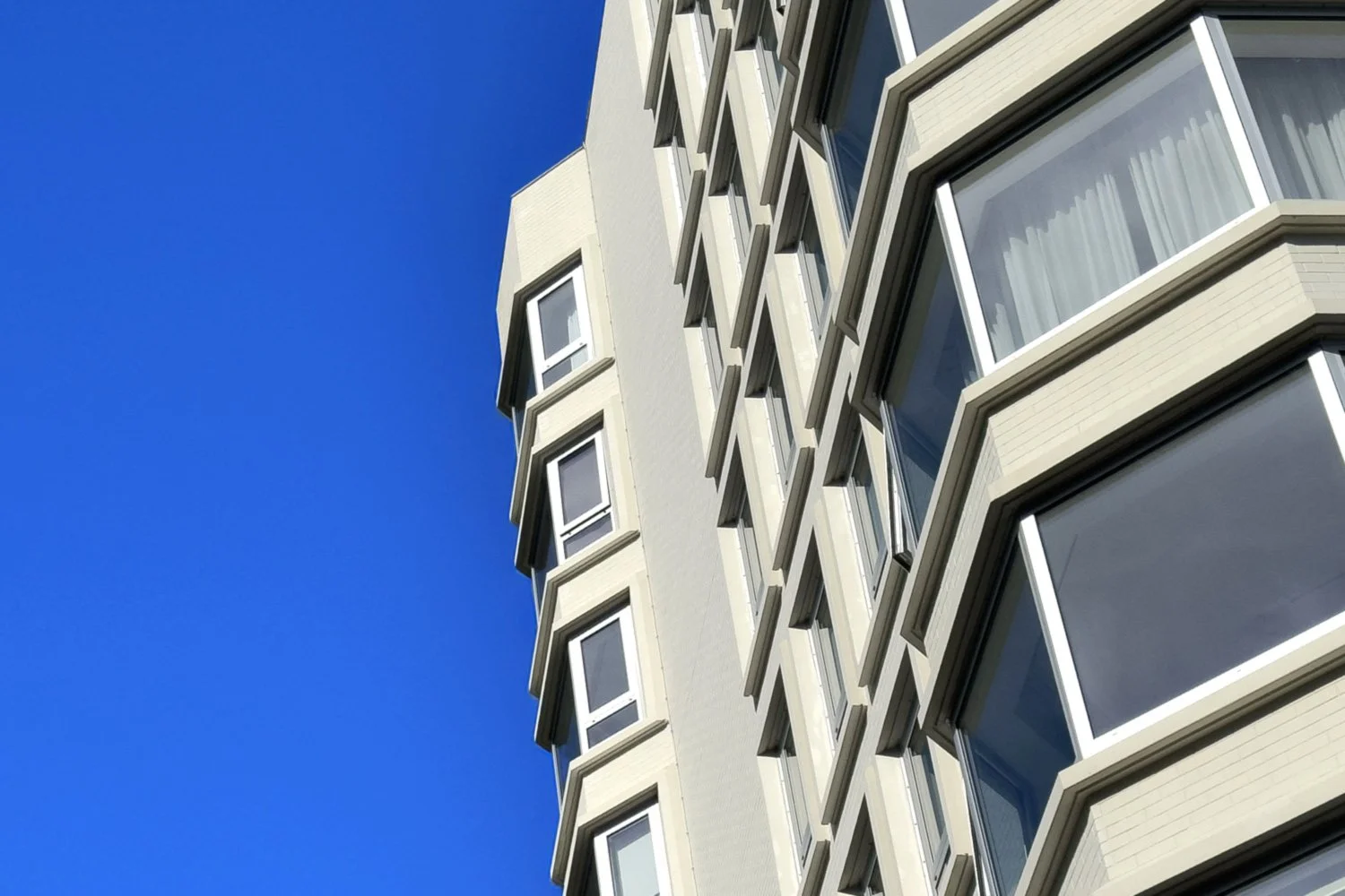 Close-up of a modern multi-story building with large windows against a clear blue sky.