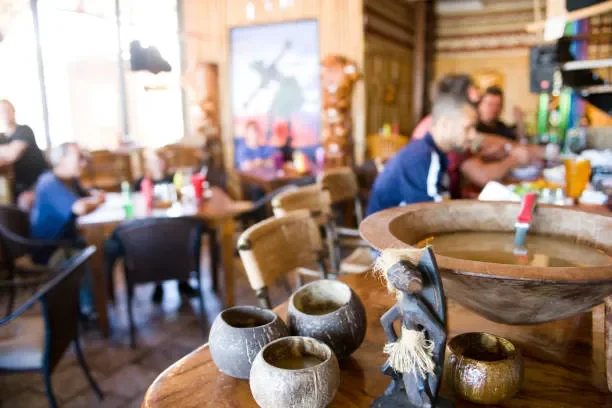 A restaurant with wooden walls and multiple tables where people are dining. In the foreground, there are clay pottery and a wooden bowl on a table.