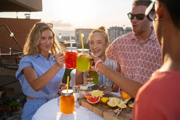 Four friends enjoying botanical teas and conversation on a rooftop patio at sunset, with snacks on the table.
