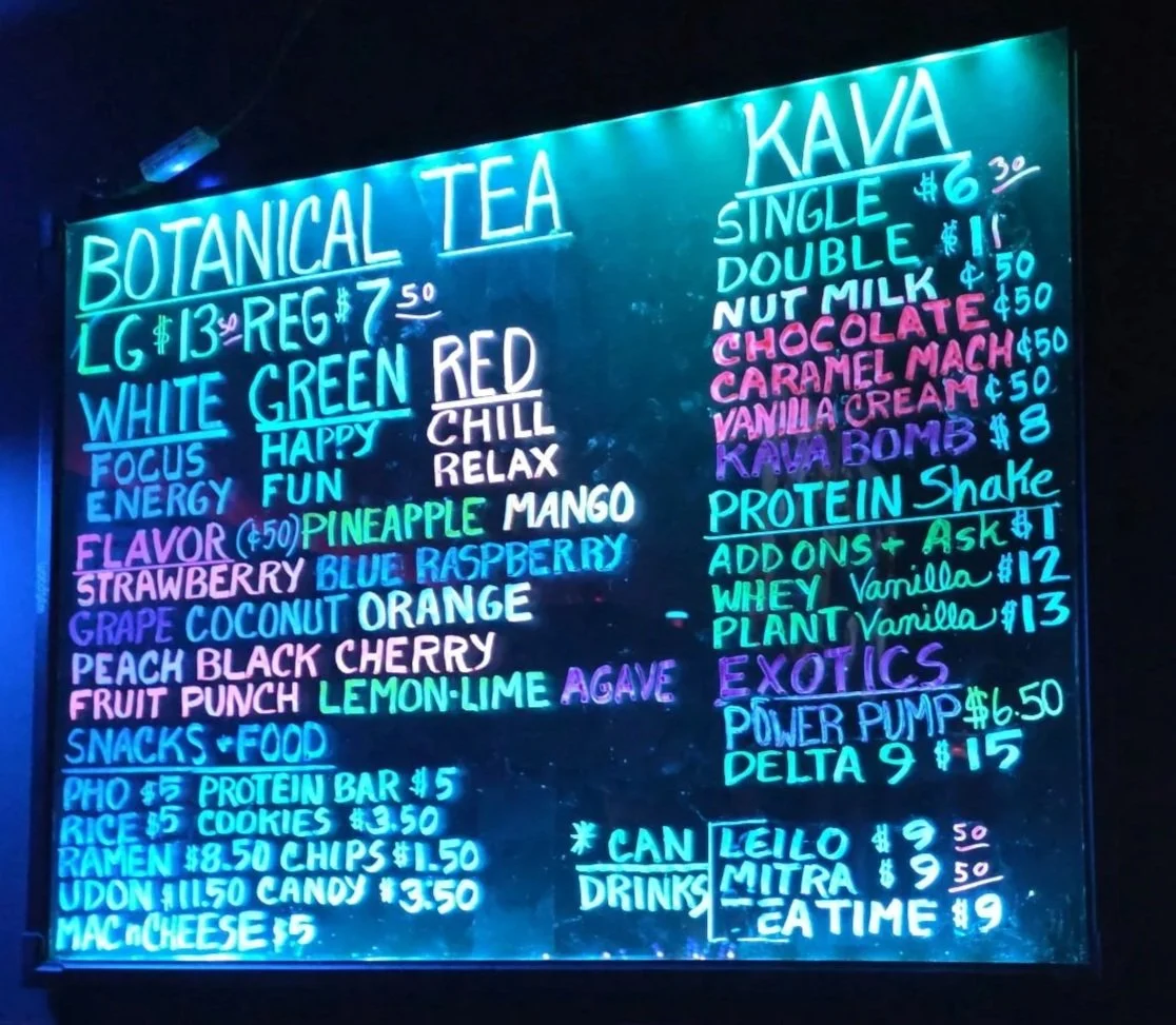 Neon blackboard menu listing various teas, flavored options, energy choices, and protein shakes.