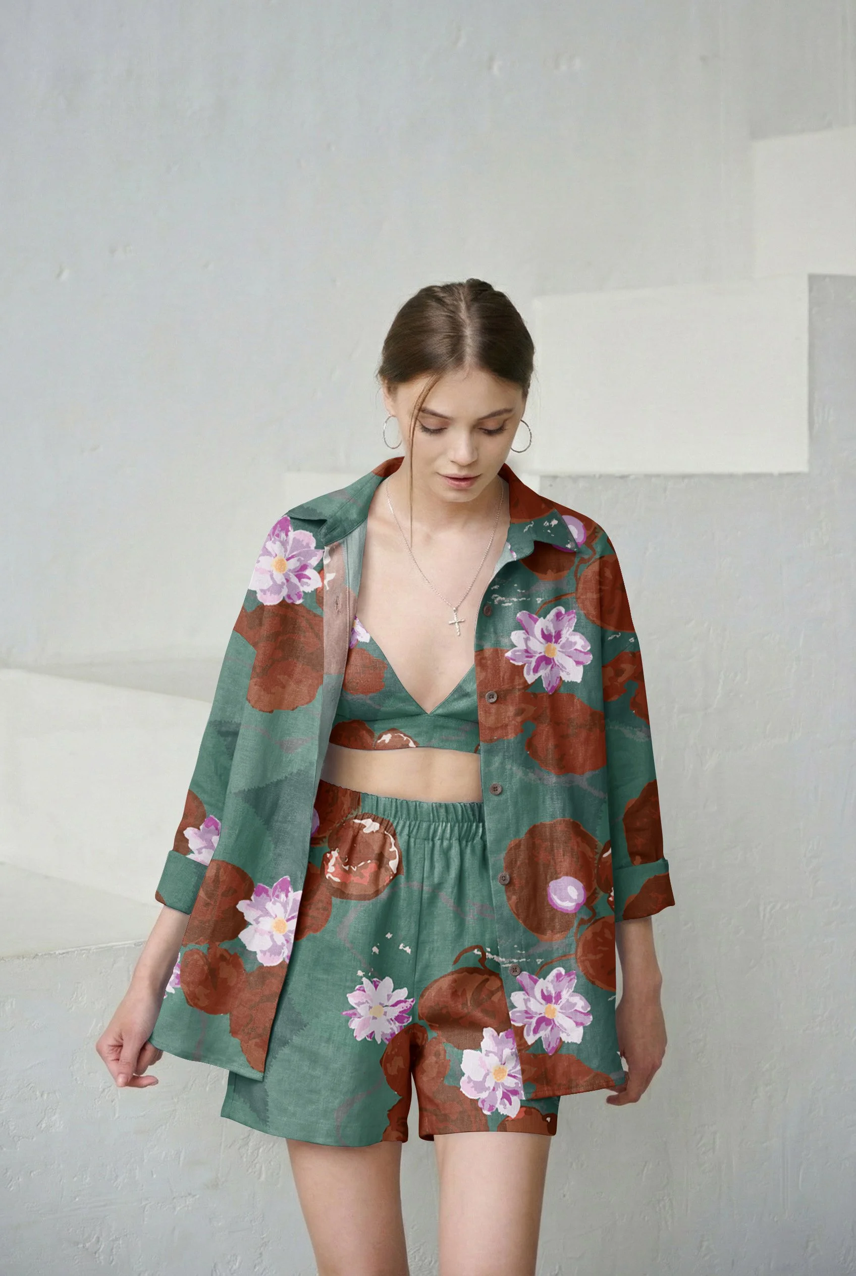 Young woman wearing matching floral green and brown outfit with purple and pink flowers, standing against a plain wall.