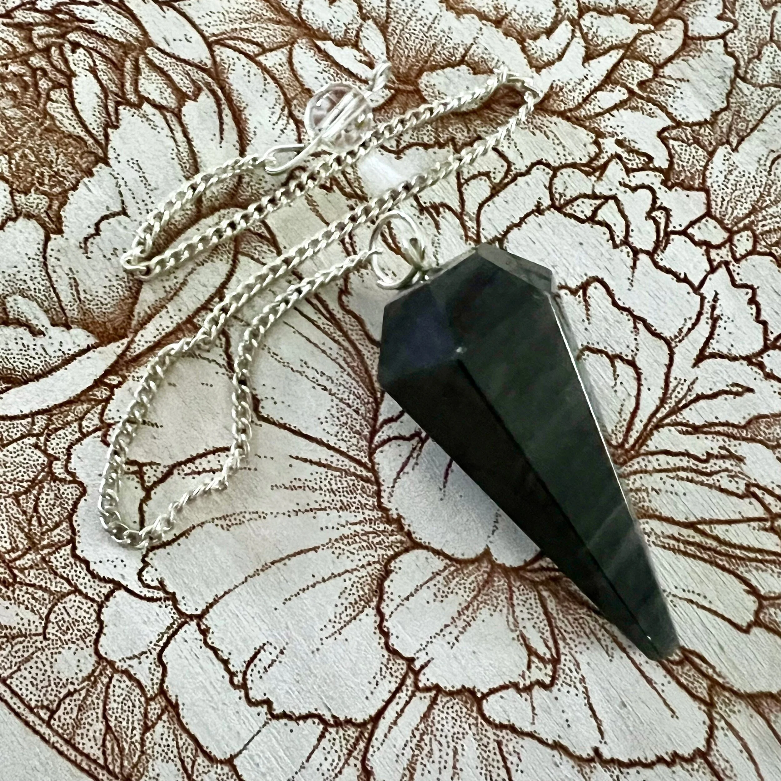 onyx pendulum on silver colored chain rests on an engraved chrysanthemum design pendulum board