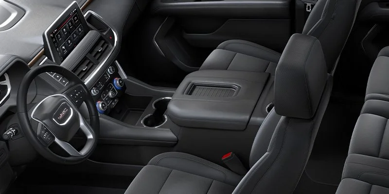The interior of a modern vehicle showing the driver's seat, steering wheel, dashboard with touchscreen display, center console with storage compartment, and passenger seat, all in a sleek, black design.