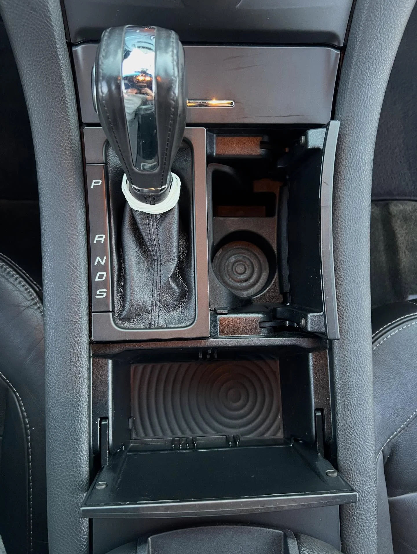 Top view of a car's center console with an automatic transmission gear shift, cup holder, and storage compartments.