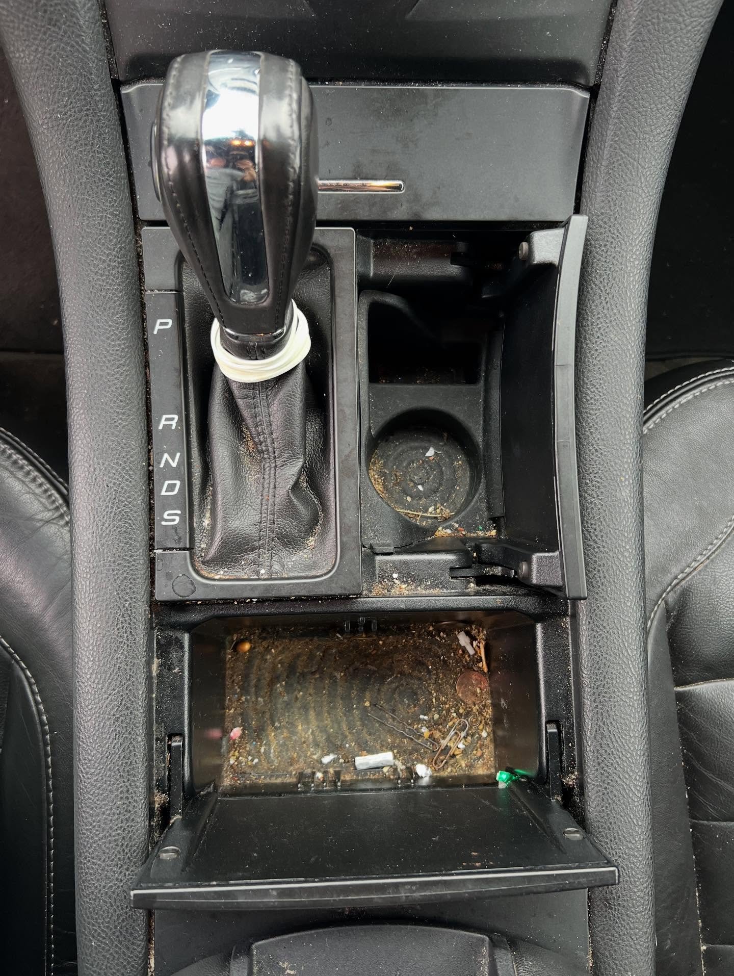 Car center console with scattered trash, dirt, and debris in the small storage compartments.