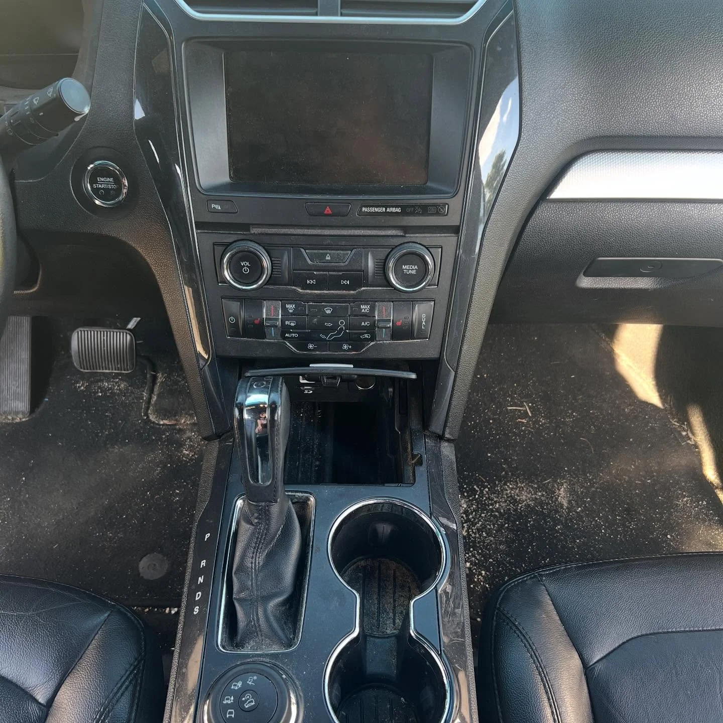 Interior of a vehicle showing the center console with gear shift, cup holders, climate controls, and a large touchscreen display.
