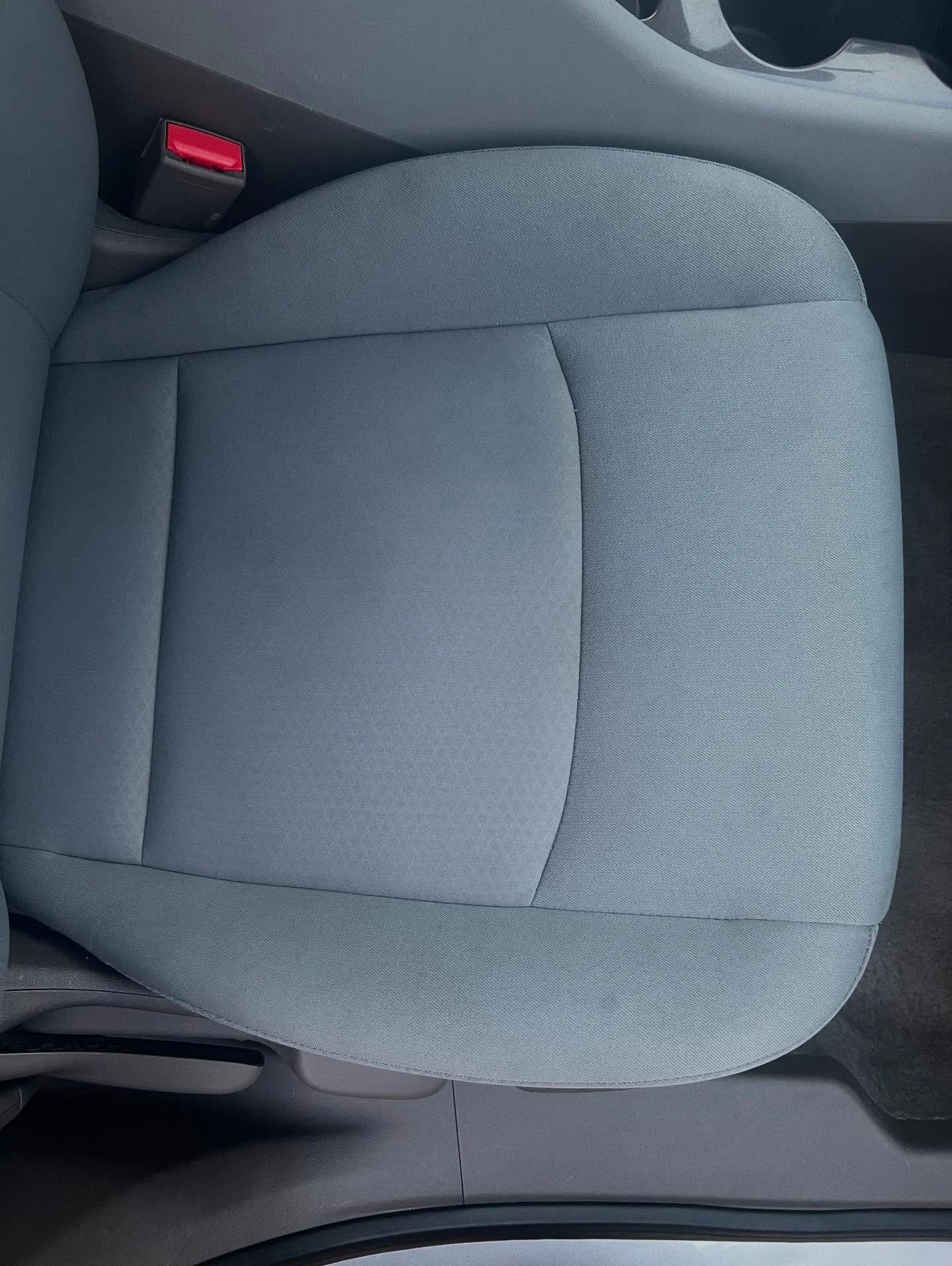 Close-up image of a gray car seat with a seat belt latch nearby.