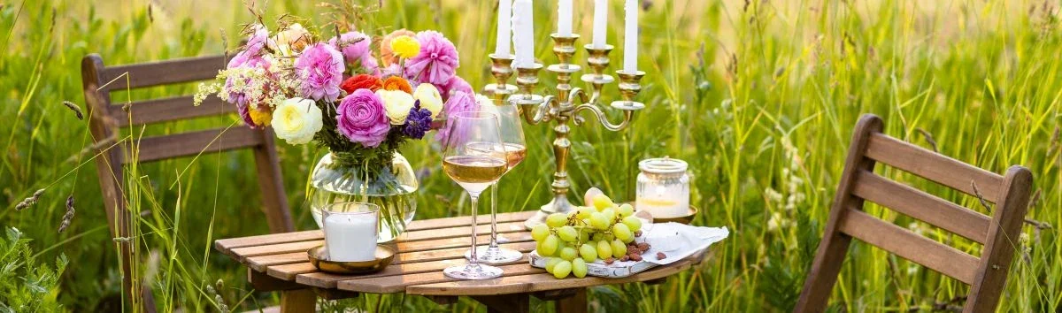 A romantic table set for two with candles, flowers, wine and grapes in a wild field.