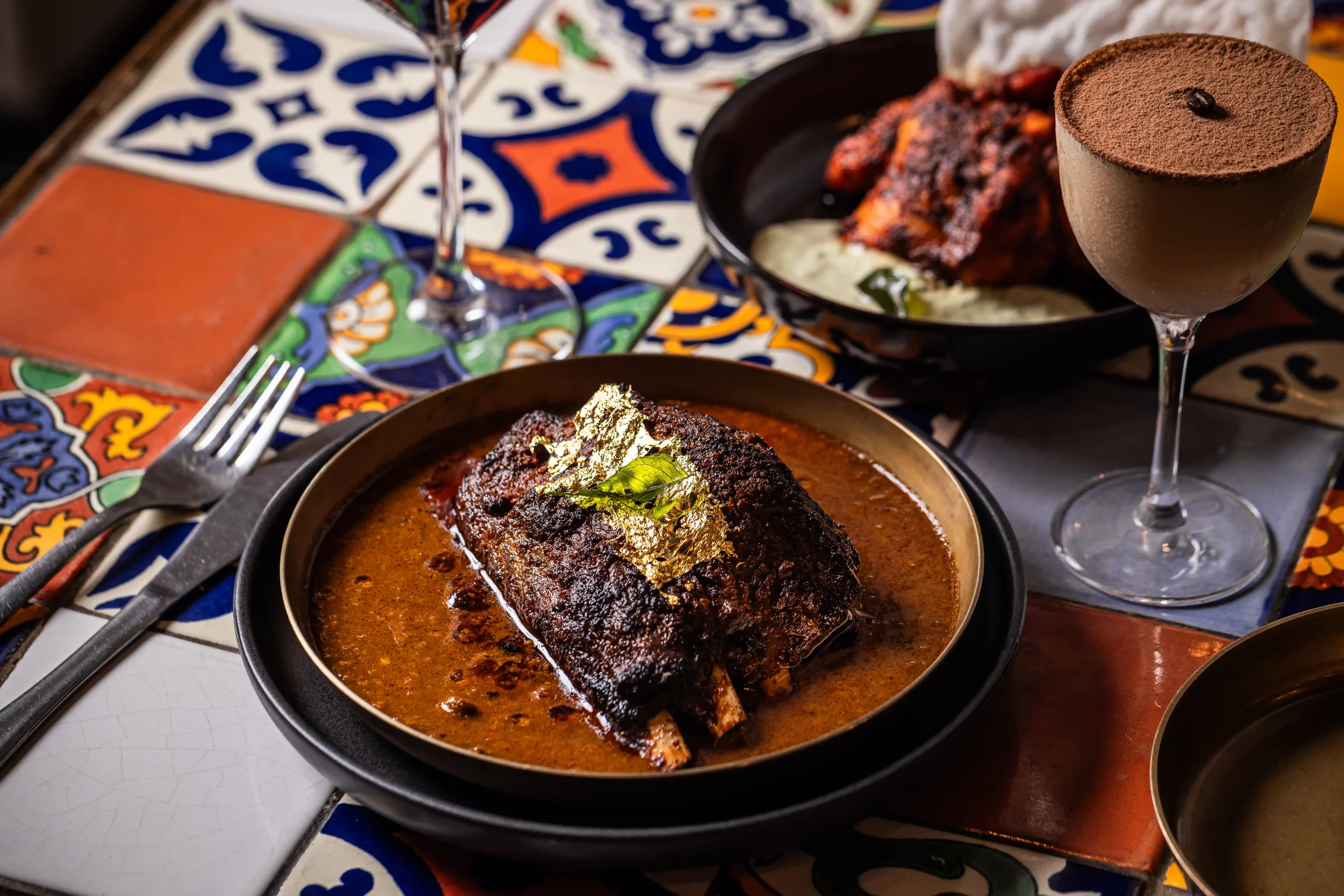 A Mexican meal with grilled fish, rice, and vegetables, served with red wine and a chocolate mousse dessert, on colorful traditional tiles