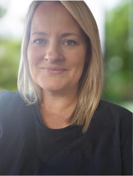 Lisa Lihou Naturopath with shoulder-length blonde hair, wearing a black shirt, smiling softly with a blurred green outdoor background.