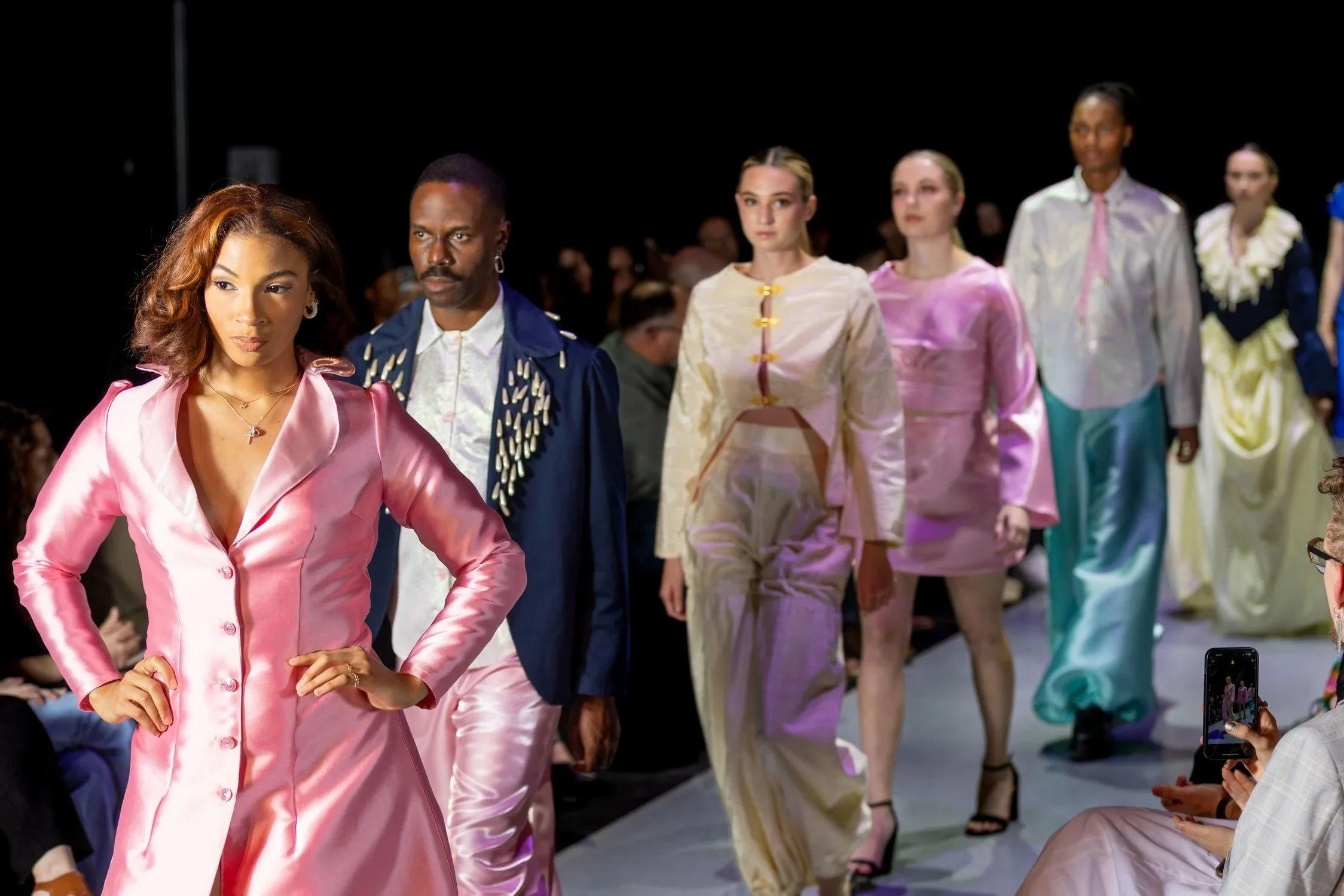 Models walking down the runway during a fashion show, wearing colorful, stylish satin outfits.