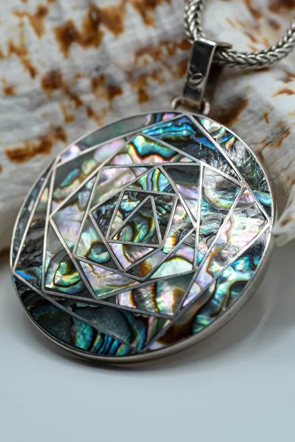 A silver necklace with a round pendant featuring an intricate spiral design embedded with iridescent mother of pearl inlays.