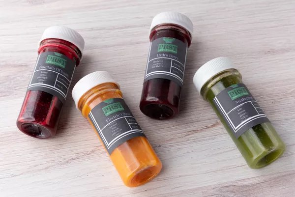 Four small bottles of paint in red, orange, dark red, and green colors placed on a light wooden surface.