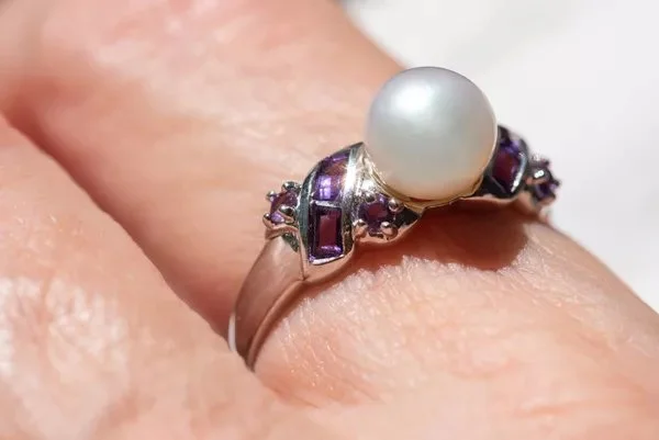 Ring with a large white pearl and small purple gemstones worn on a finger.