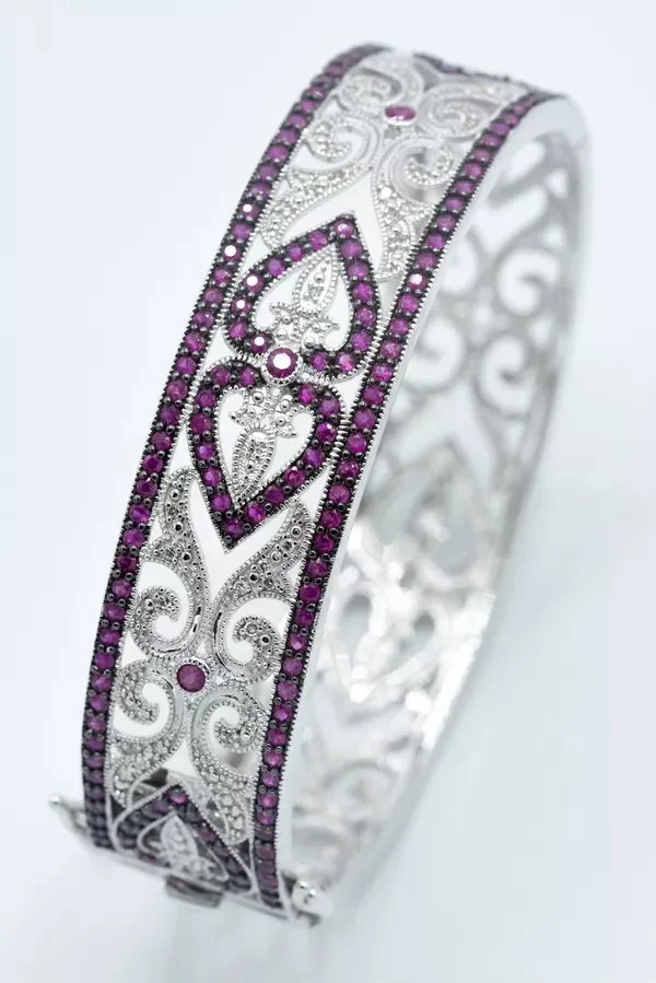 Silver bracelet with intricate filigree work, decorated with purple gemstones along the edges and within the design.