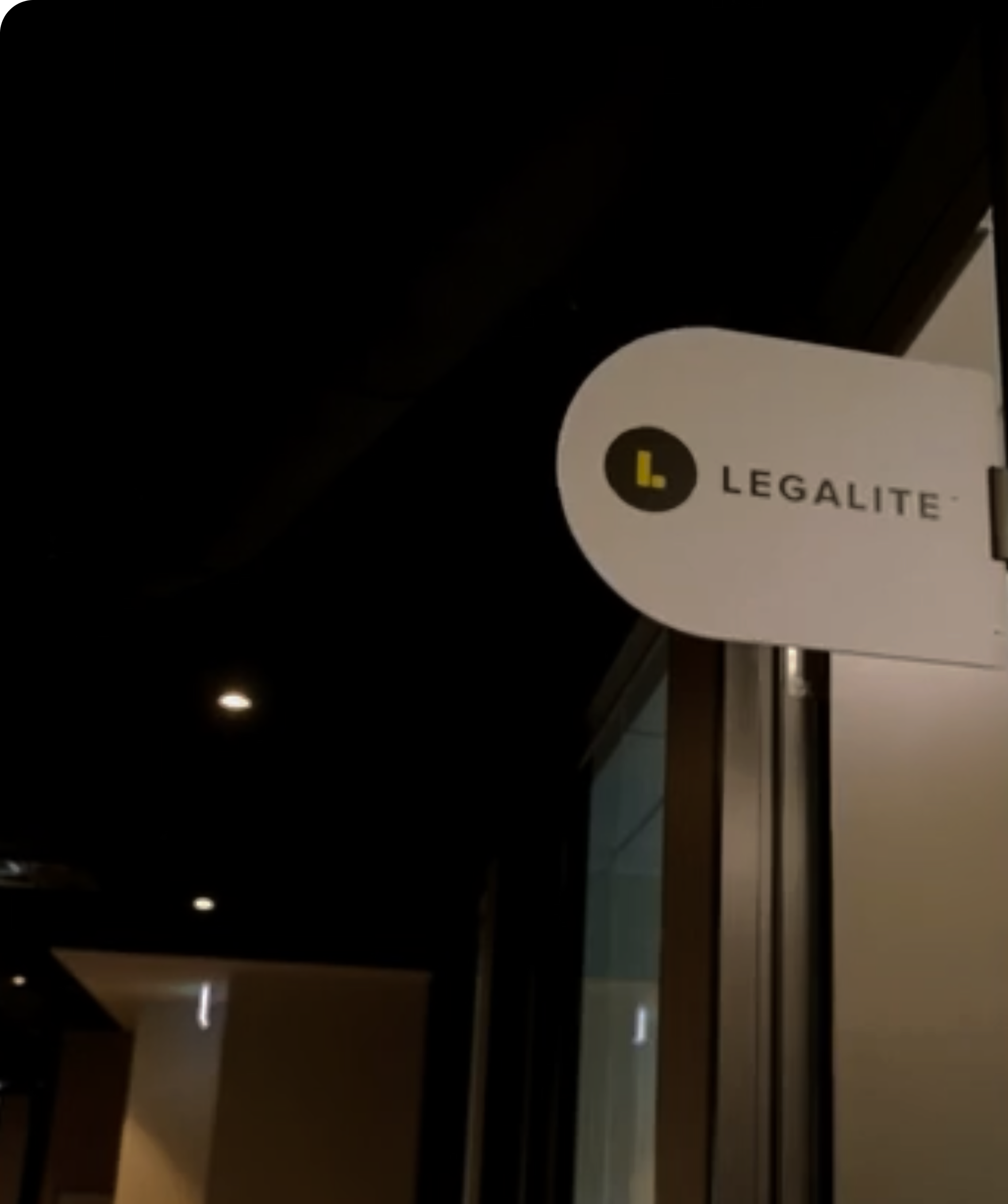 Signboard for Legalite with a yellow and black logo showing a large white 'L' inside a black circle, and the text 'LEGALITE' in black, mounted on a building at night.
