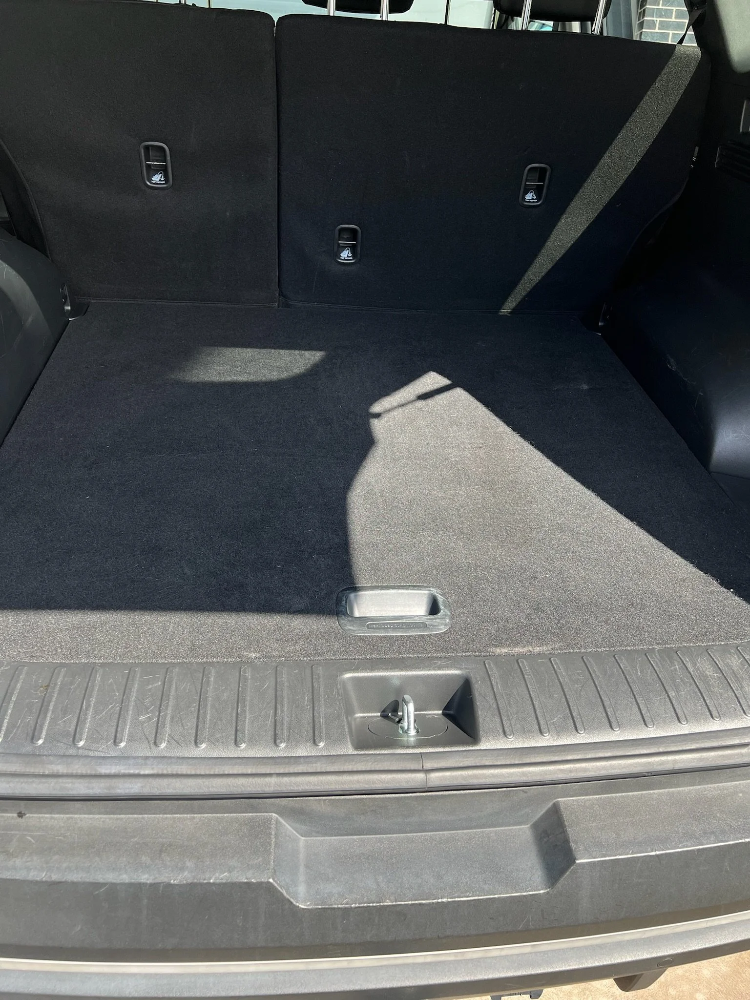 Empty car trunk with black interior and a gray exterior, showing a latch and lock mechanism at the bottom.