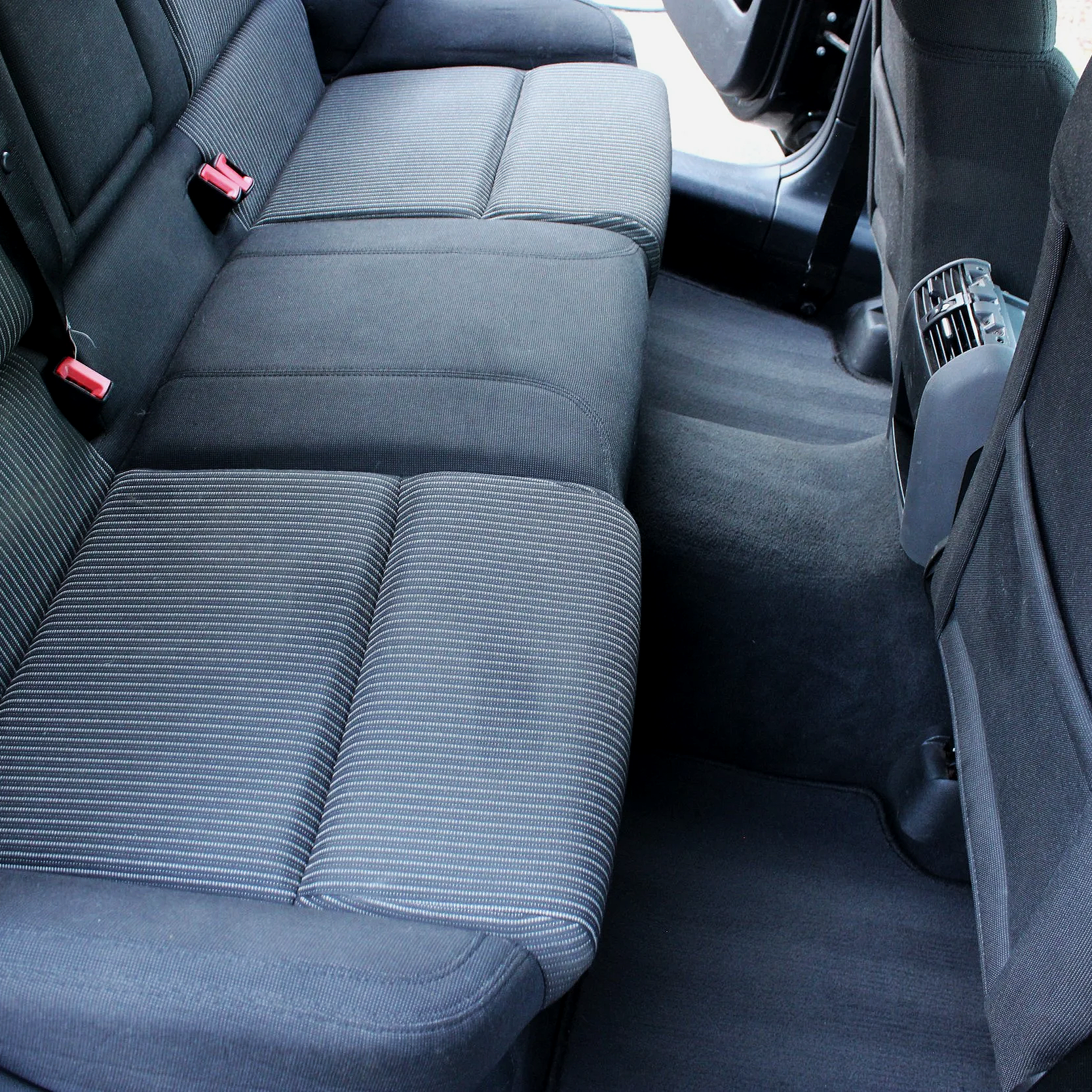 The backseat of a car showing three striped fabric seats, seatbelts, and the rear of the front seats with vents and a storage pocket.