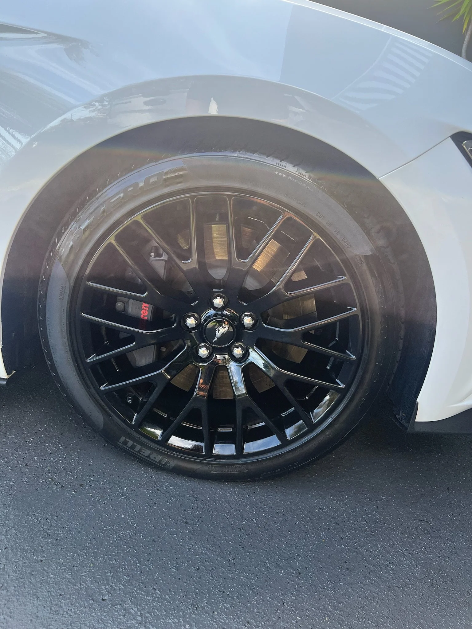 Close-up of a Tesla car's front wheel with black rims and red brake caliper, on a black asphalt surface.