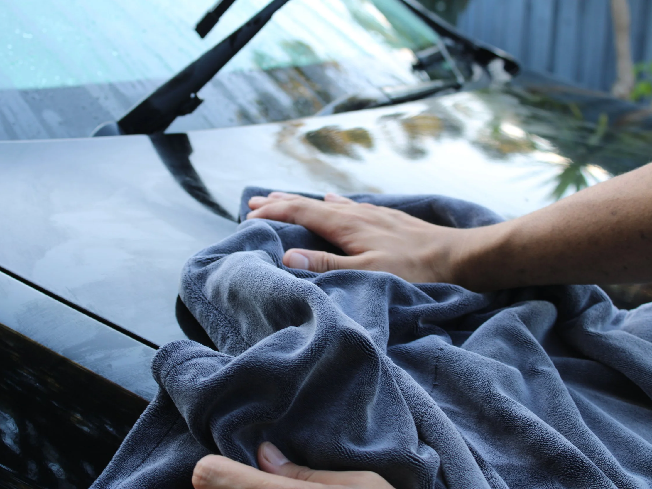 A person cleaning the hood of a black car with a gray cloth.