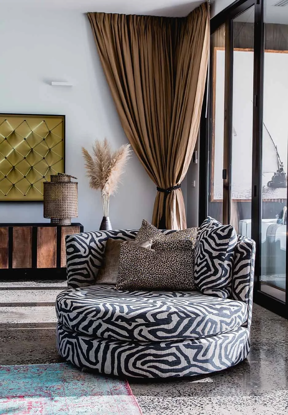 Curved statement armchair in bold animal print with layered cushions, set beside floor-length curtains in a warm, textured living space
