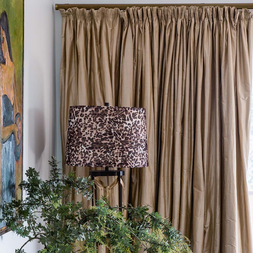 Interior detail featuring gathered silk curtains, patterned table lamp and greenery creating a rich, textural styling moment