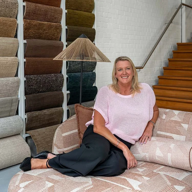 Interior designer Sally Wilson seated in her studio surrounded by fabric samples and material boards, smiling in a relaxed, welcoming environment