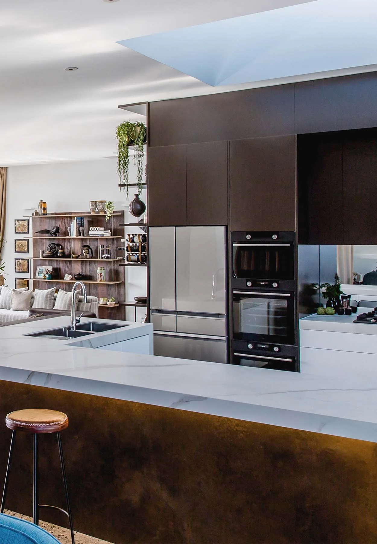 Open-plan kitchen with dark timber cabinetry, stone island bench and seamless connection to a styled living area with shelving and decor