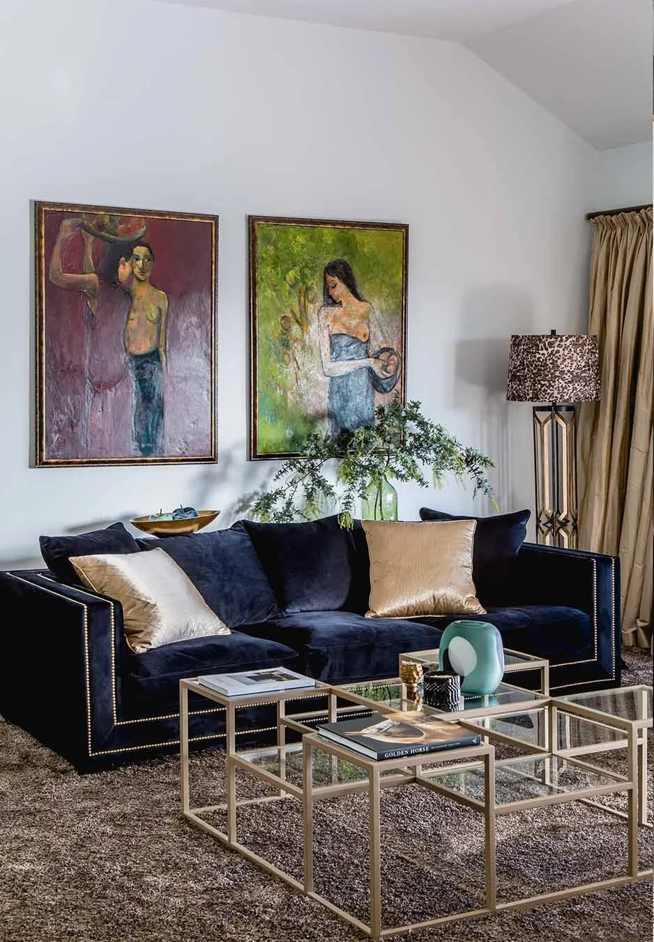 Living room with deep navy velvet sofa, glass coffee tables and large framed artwork creating an elegant, layered interior setting