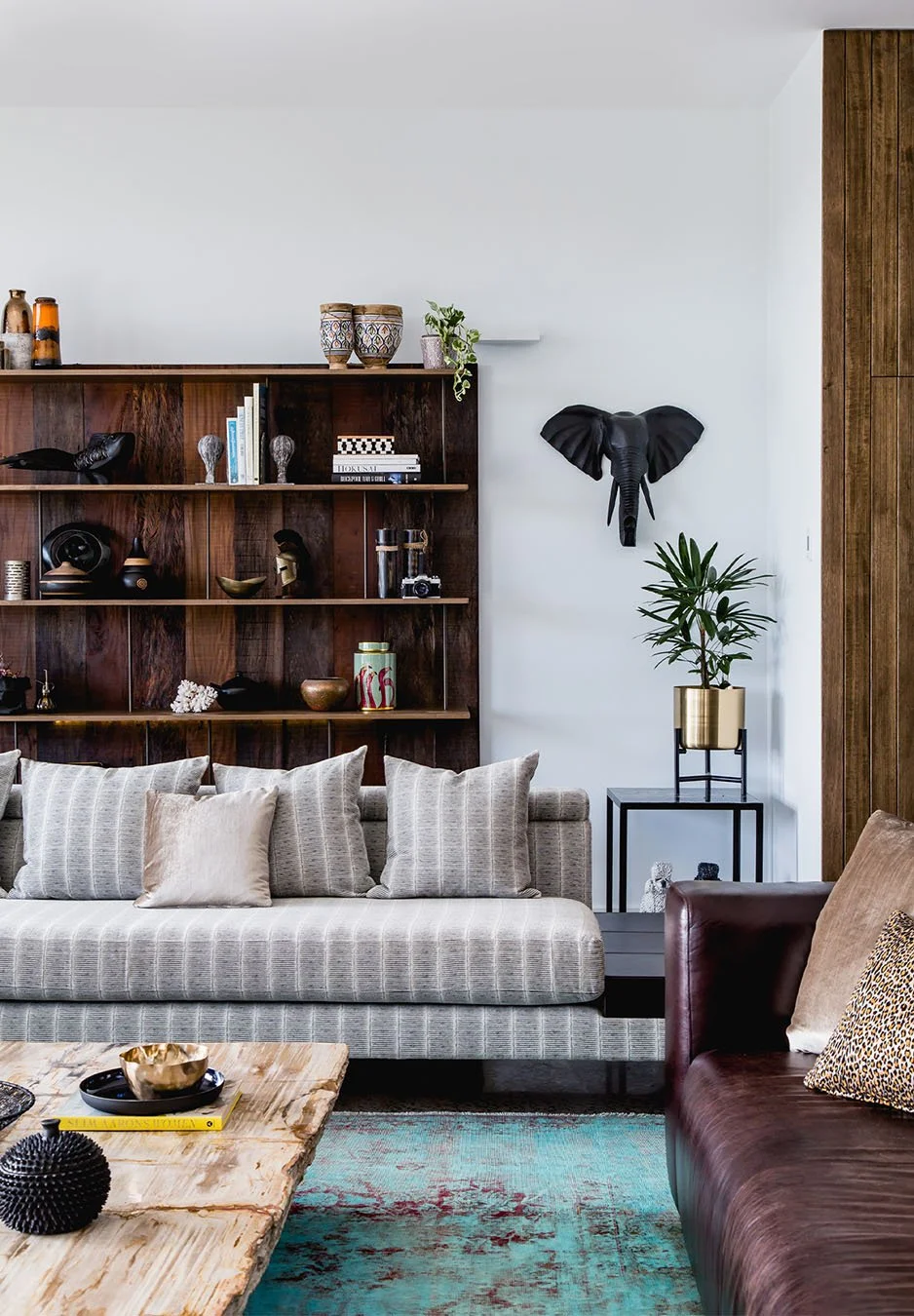 Refined living room with neutral sofa, timber shelving styled with objects and books, leather armchair, marble coffee table and layered textures creating a warm, considered interior.