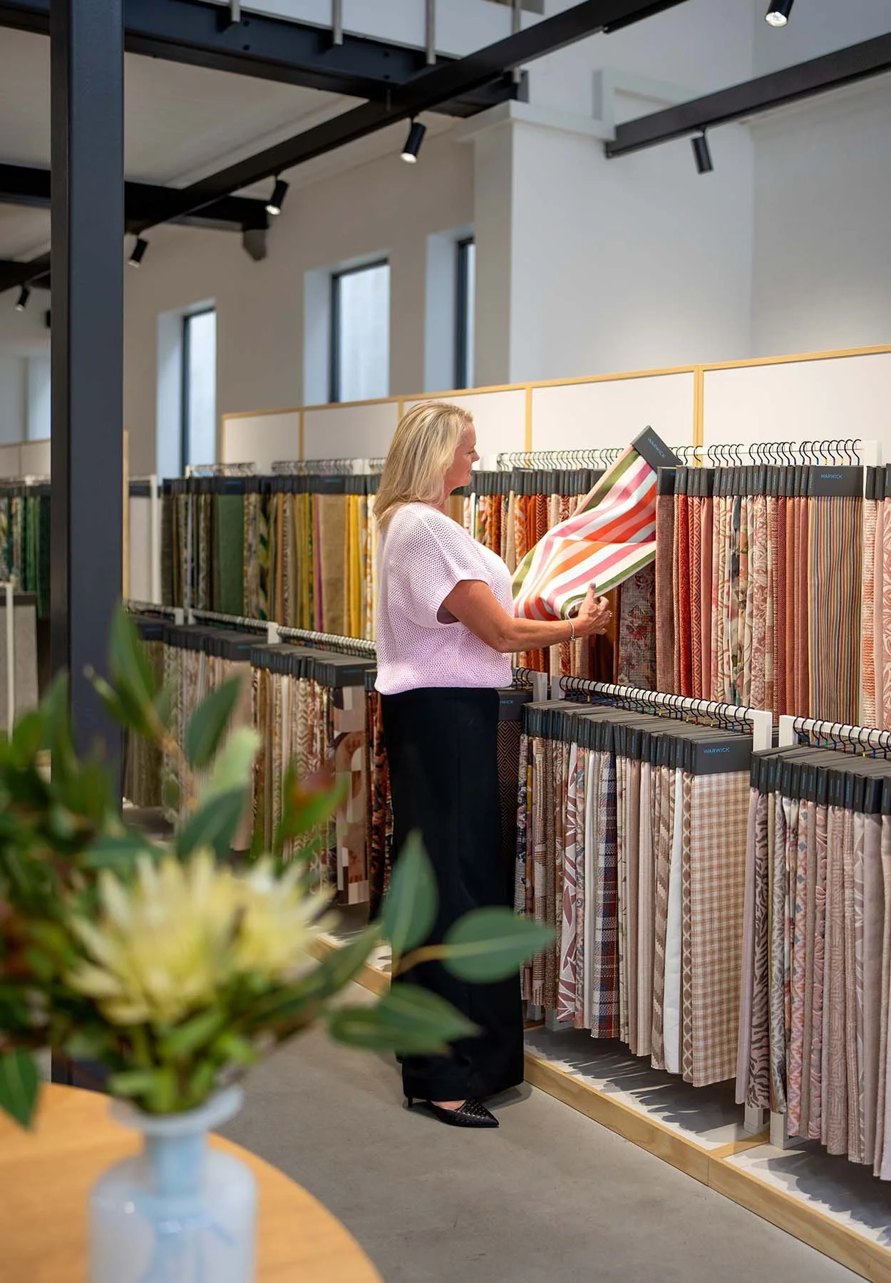 Interior designer reviewing fabric samples in a textile showroom, selecting patterned and textured materials for a residential design project.