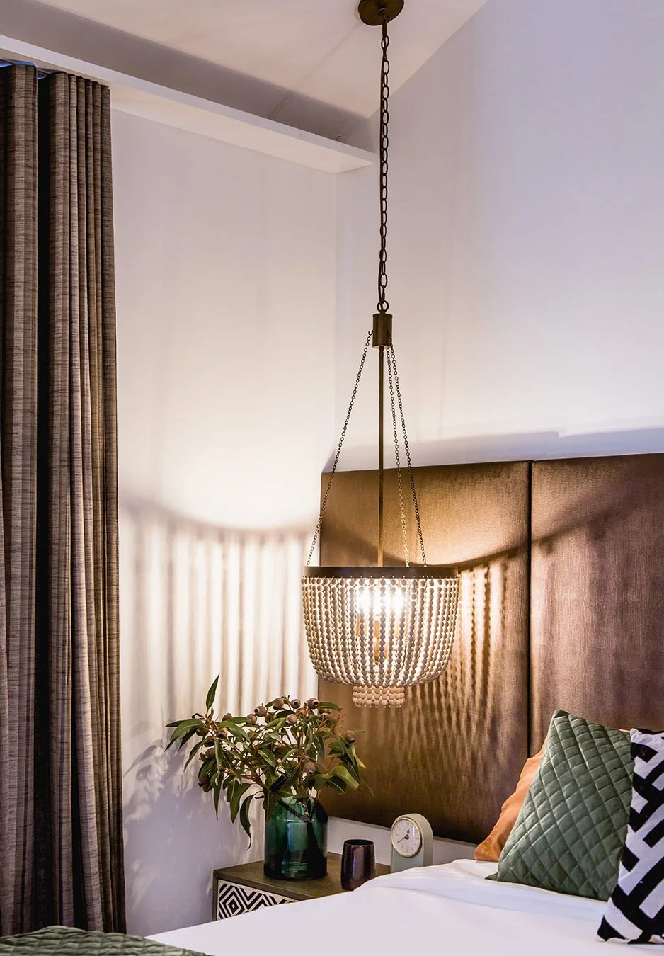 Bedroom detail with pendant light, upholstered headboard, layered cushions and soft lighting creating a warm, intimate atmosphere