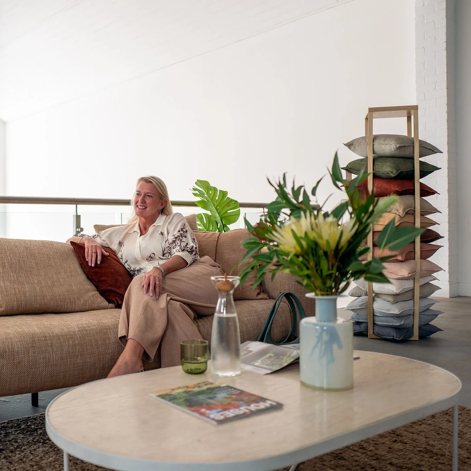 Interior designer Sally Wilson seated on a sofa in a relaxed living space, surrounded by soft furnishings, greenery and natural textures