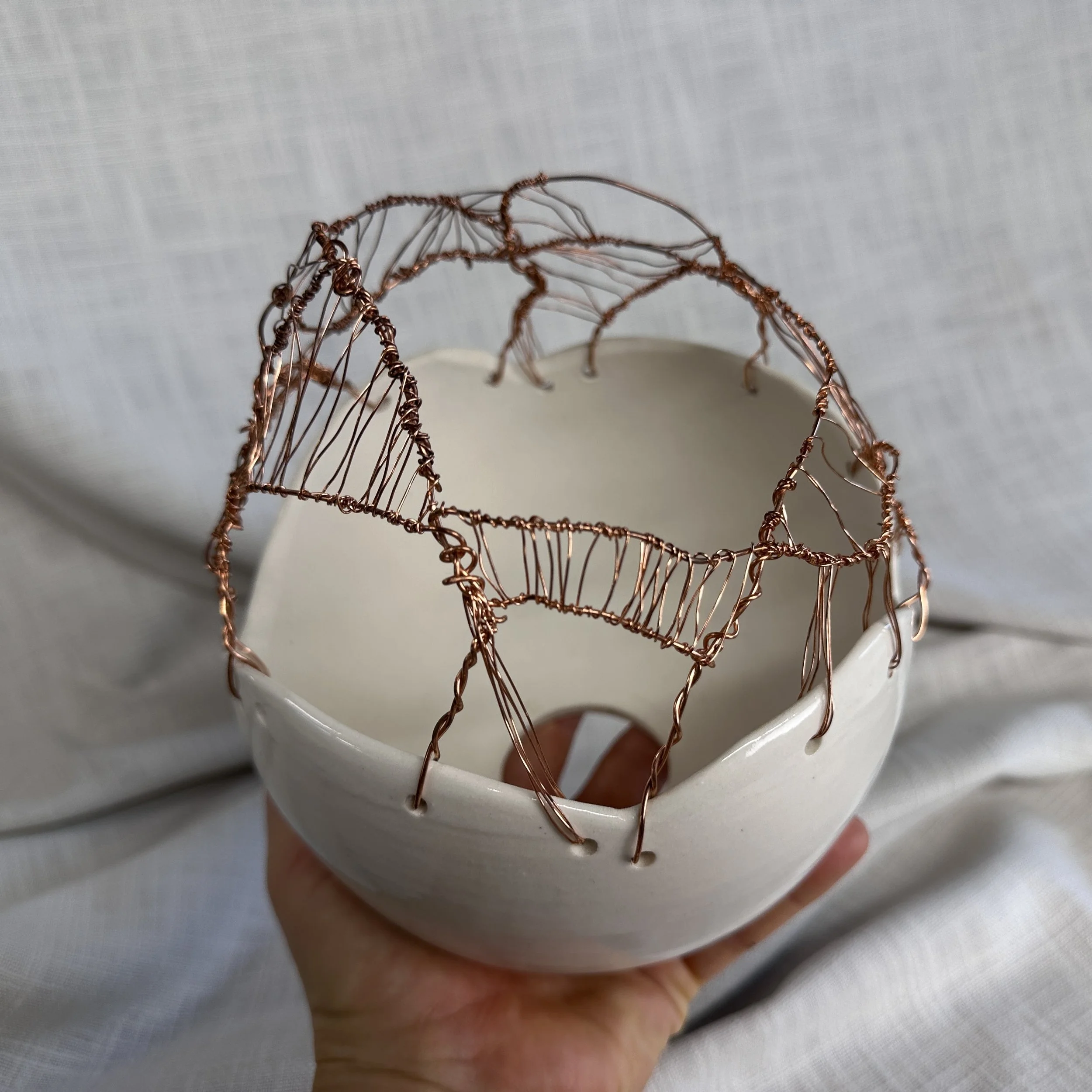 A white ceramic pendant lampshade with a decorative copper wire structure designed to reflect the light when turned on.