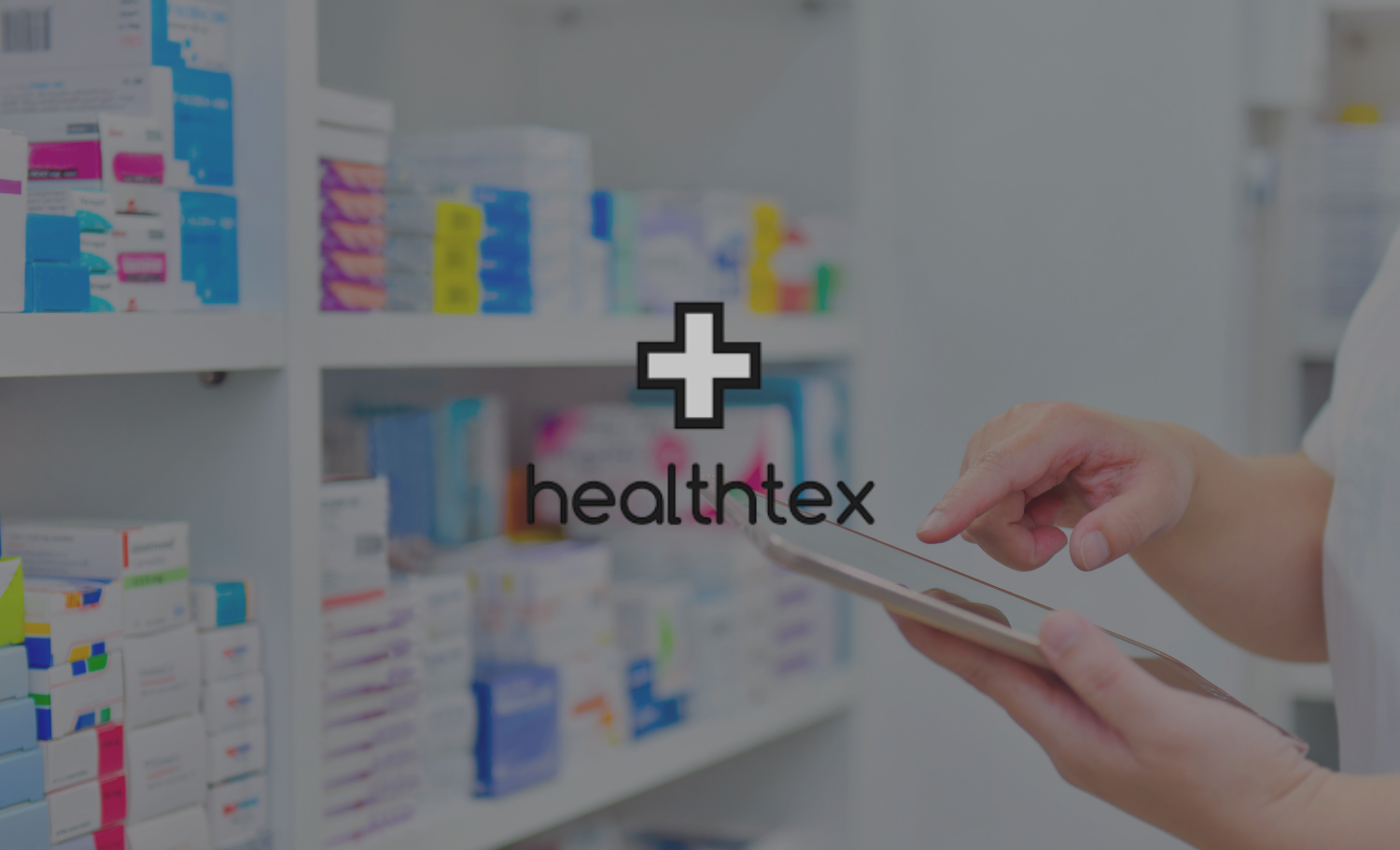 A healthcare professional using a tablet in a pharmacy with shelves of medication in the background.