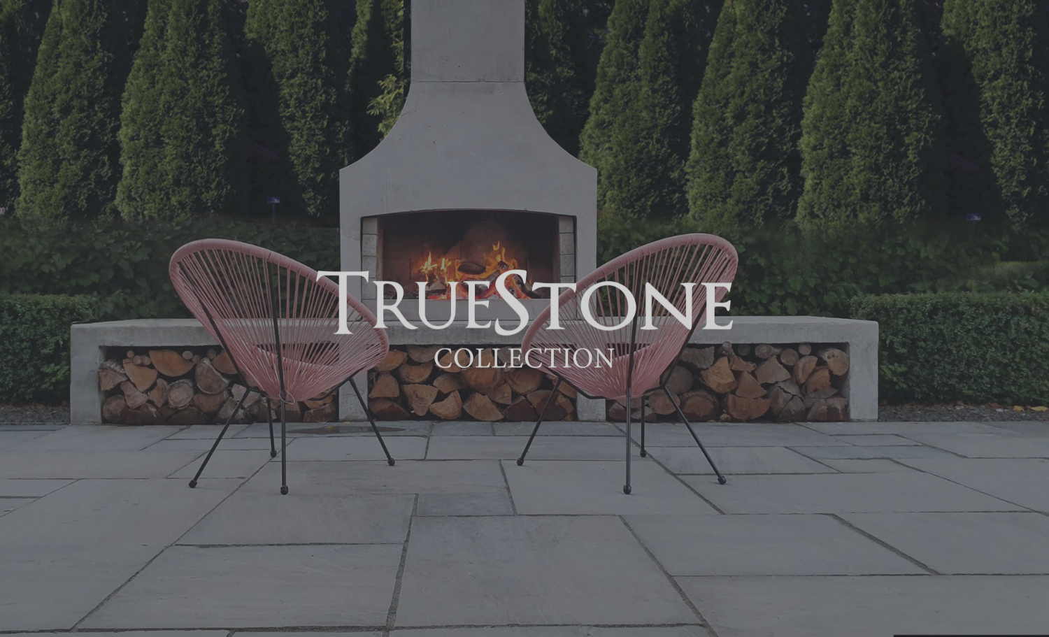 Outdoor patio with two pink chairs in front of a stone fireplace, surrounded by greenery, with the text 'TRUESTONE COLLECTION' overlayed.