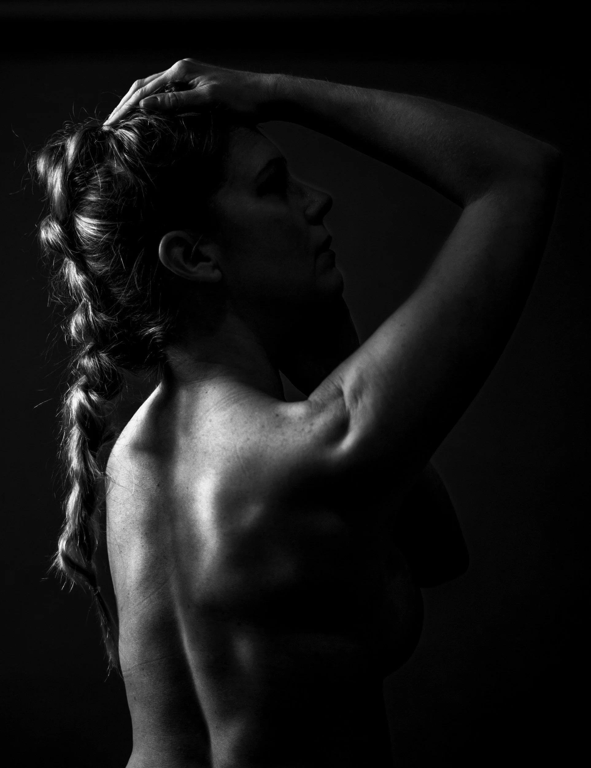 Black and white photo of a woman with braided hair, her eyes closed, with one arm raised, touching her head.