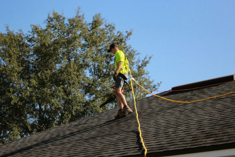 Commercial roofing technician inspecting asphalt shingle roof while secured with safety harness