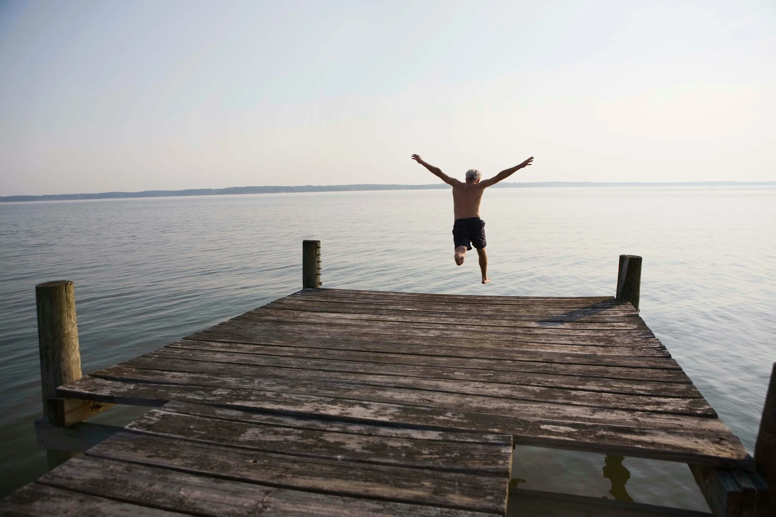 A person jumping off a wooden dock into a body of water on a clear day.