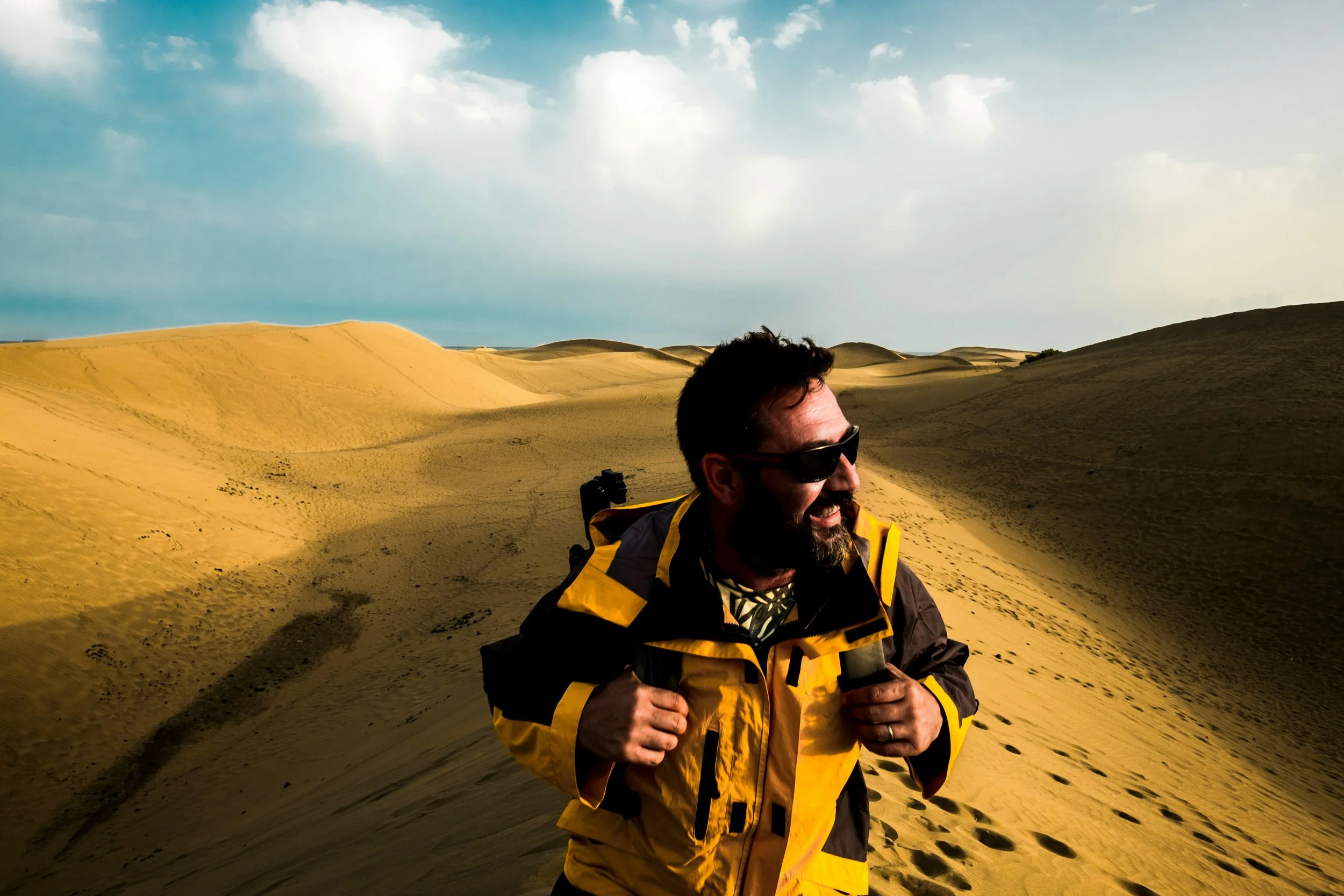 Man in yellow and black jacket with black sunglasses running through sand dunes. Physically fit man in his 50s representing the health goals Atlas Performance Pro is designed to help men achieve