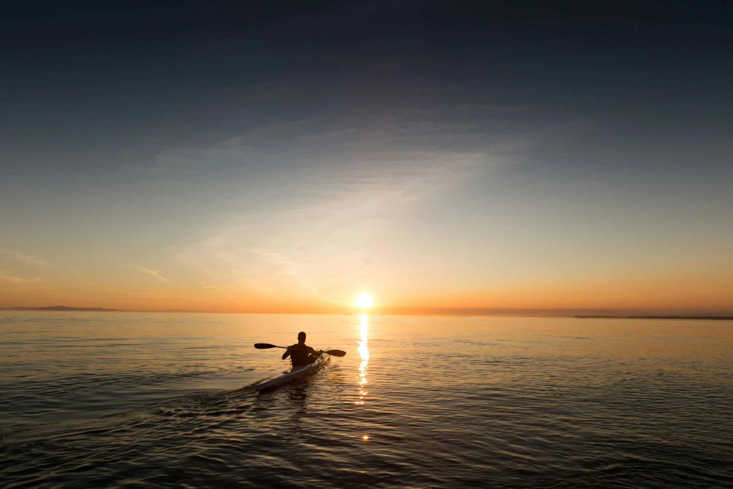 Person kayaking on calm water during sunset with a vibrant sky.