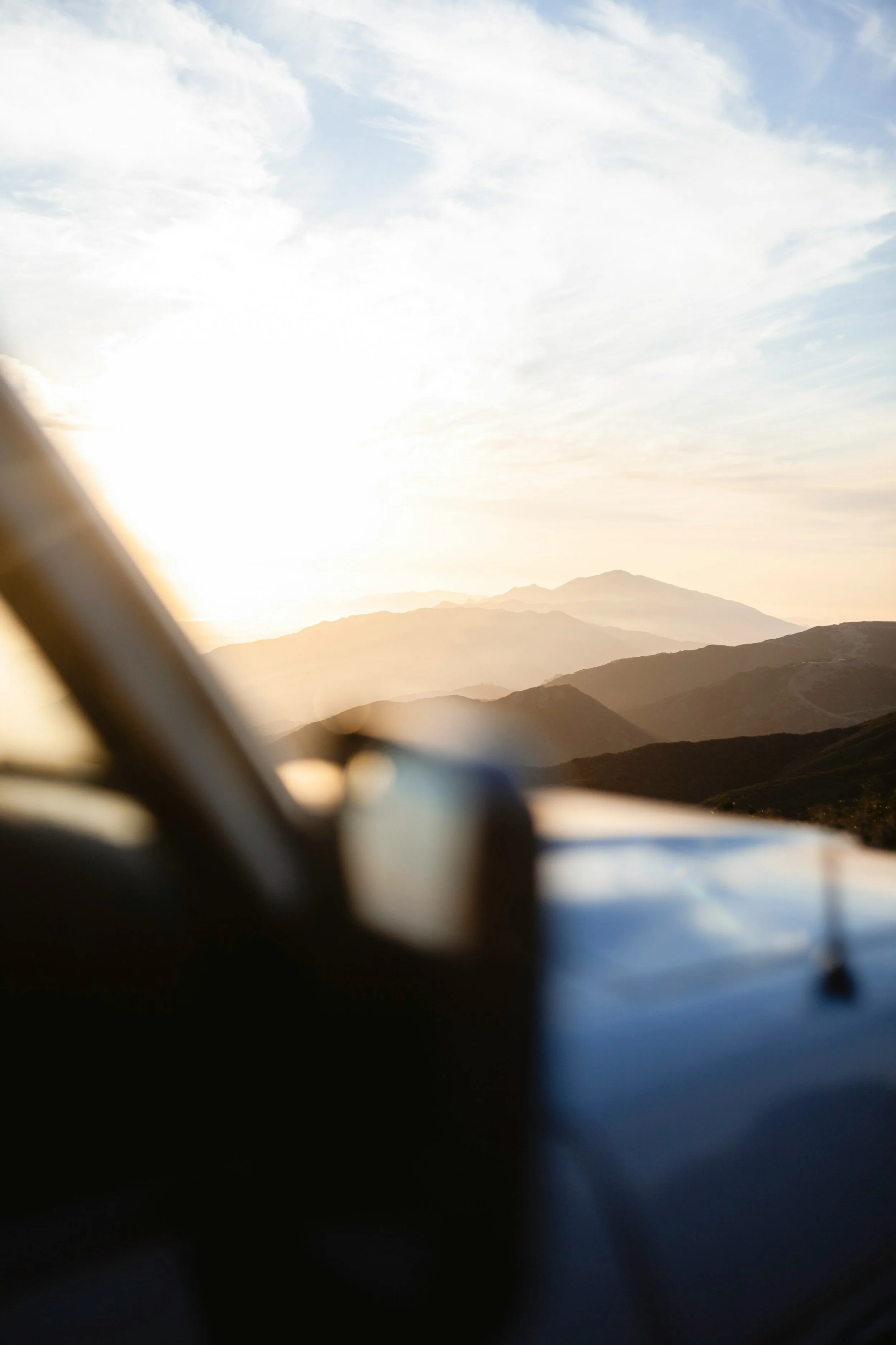 View of a mountain range and clouds seen from inside a vehicle at sunset or sunrise.