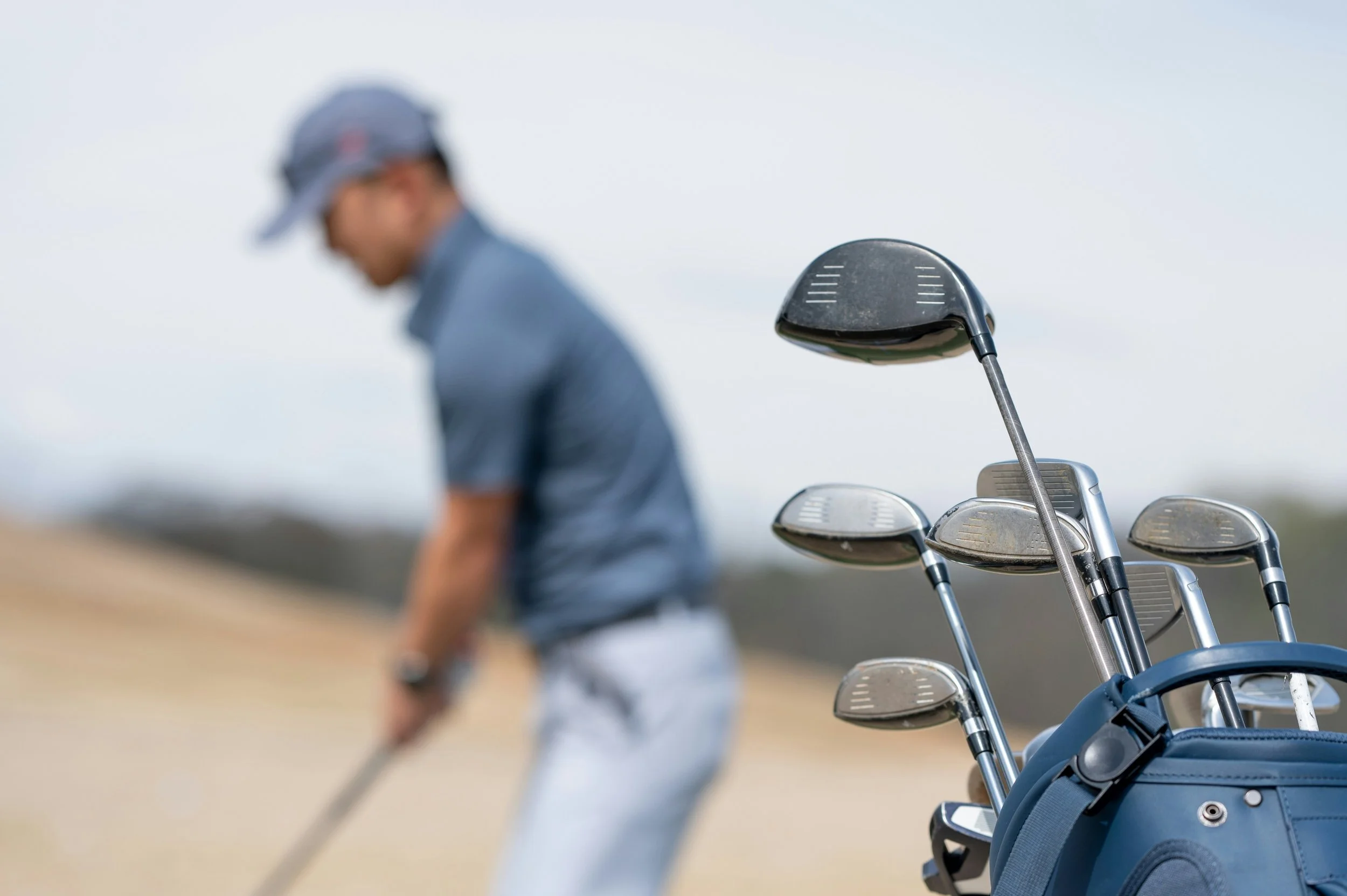 Close-up of golf clubs in a golf bag on a golf course with a golfer in the background preparing to take a shot. Man exercising and staying active after 40 — representing Atlas Formulas' approach to men's health optimization