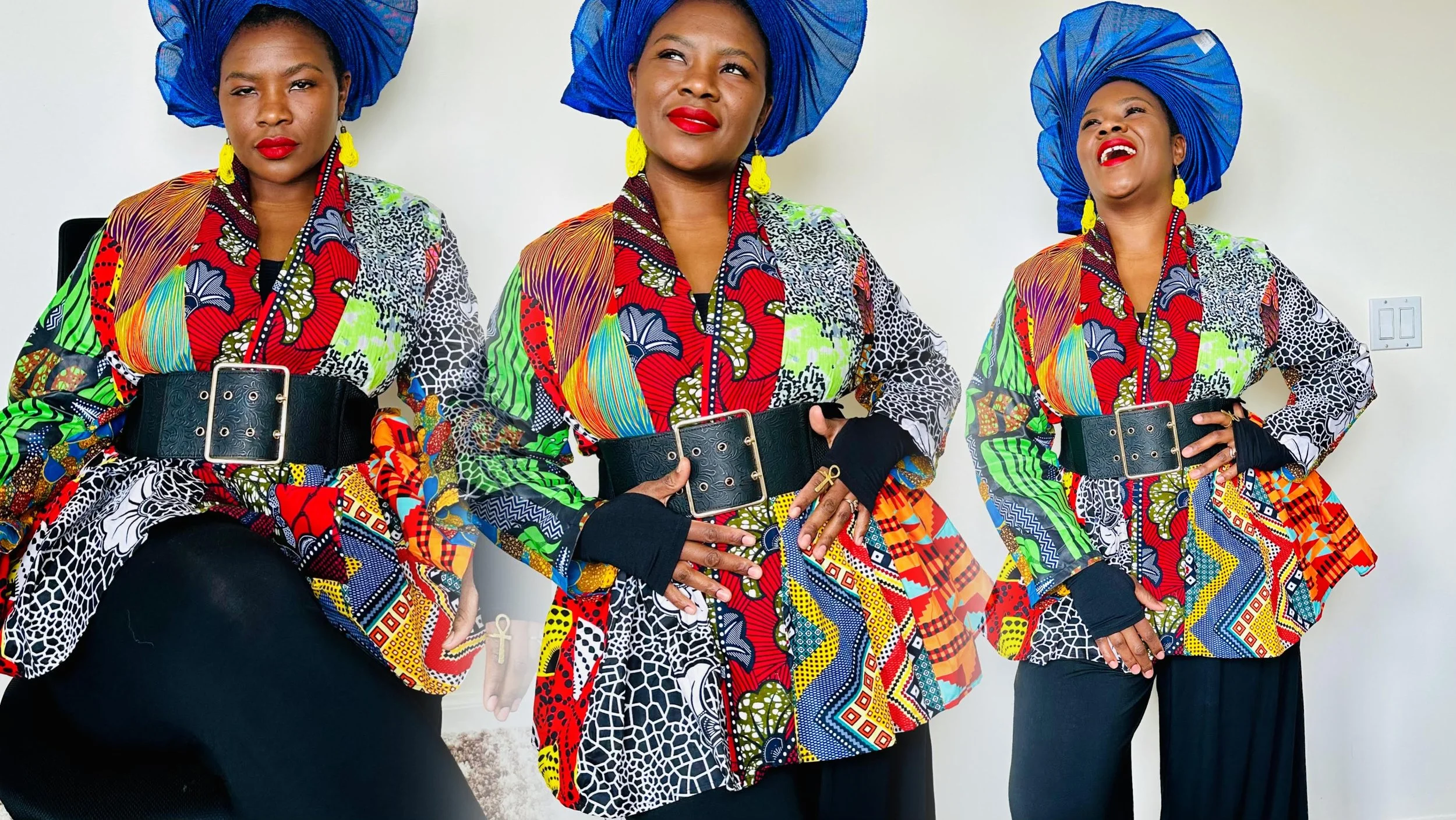 Three women wearing colorful African print outfits with large blue headwraps, standing against a plain white wall, smiling and posing.