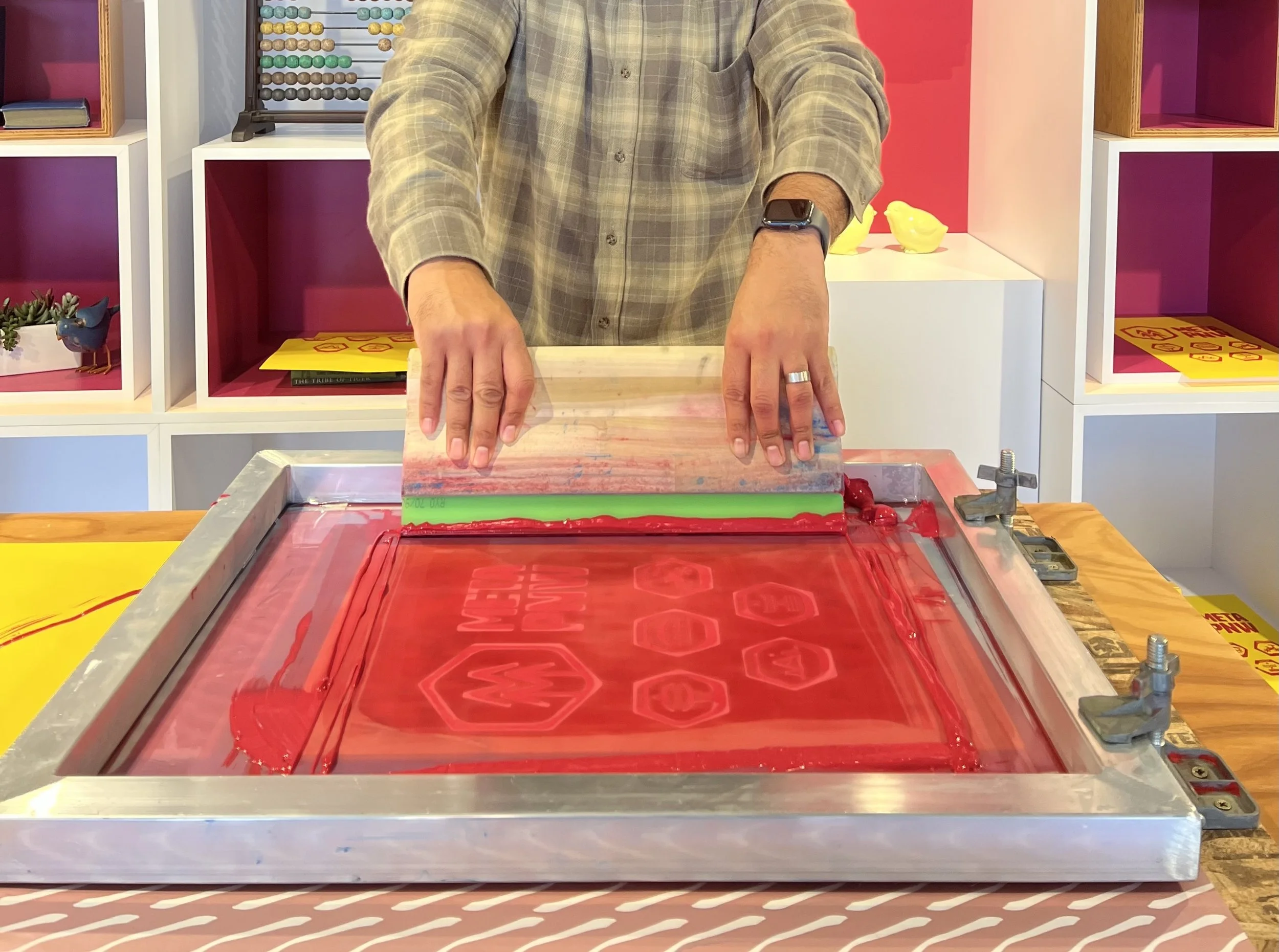 Person using a squeegee to live screen print a poster with red screen printing ink.