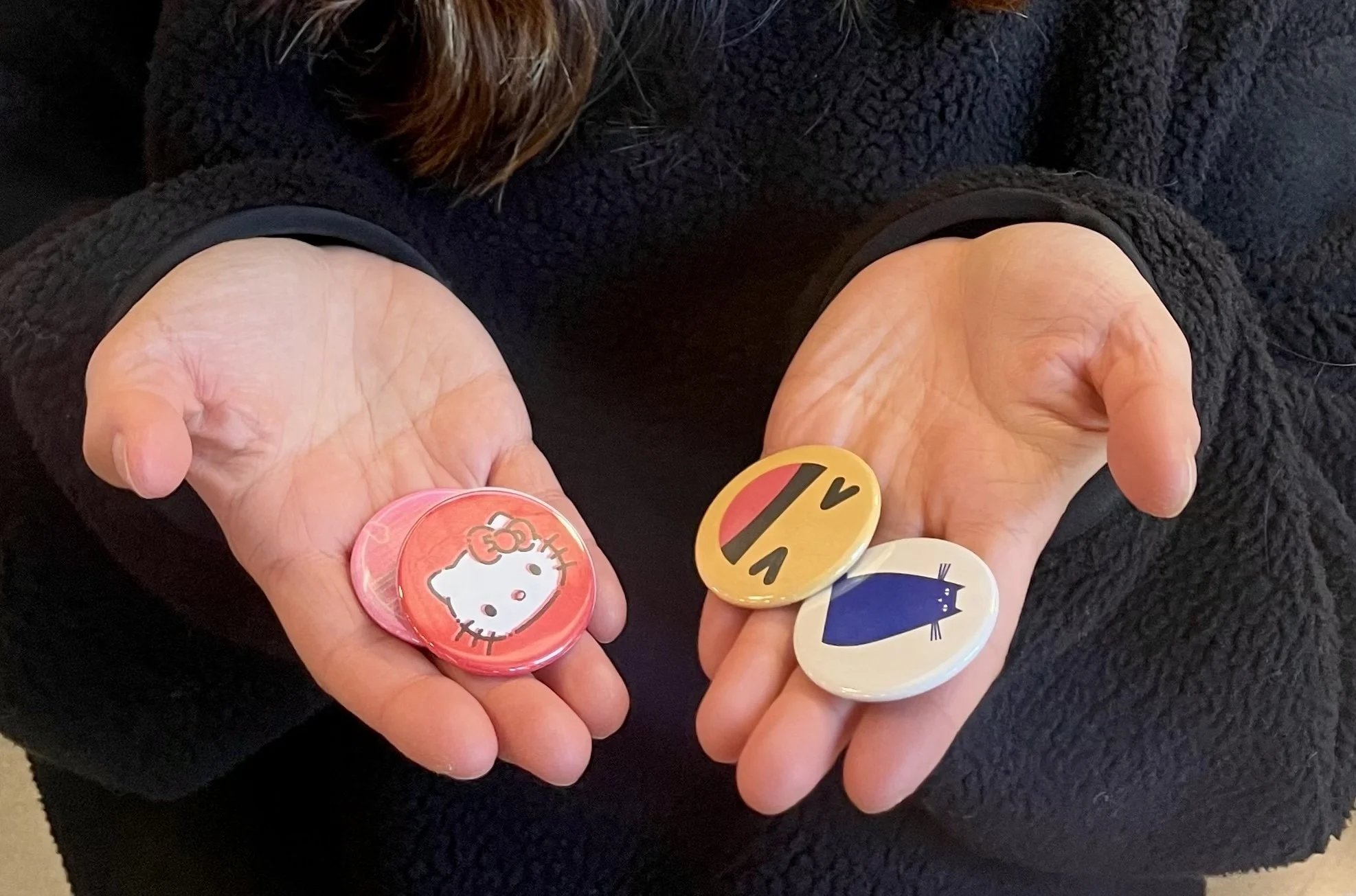 Person holding colorful buttons made at a live button making art activation that include Hello Kitty, a yellow face with sunglasses, and a blue cat illustration.