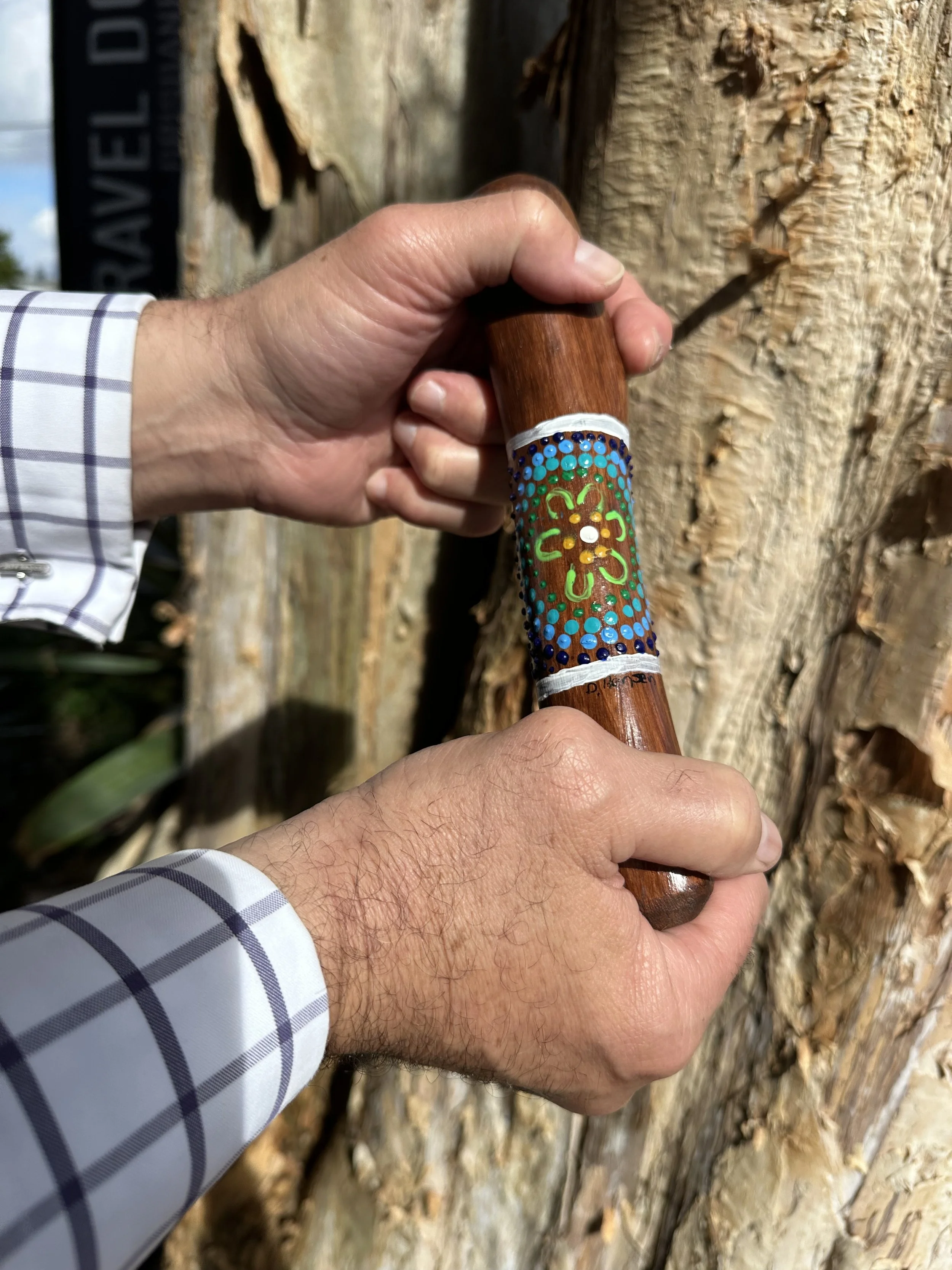 Person holding a decorated yarning stick against a tree trunk outdoors.