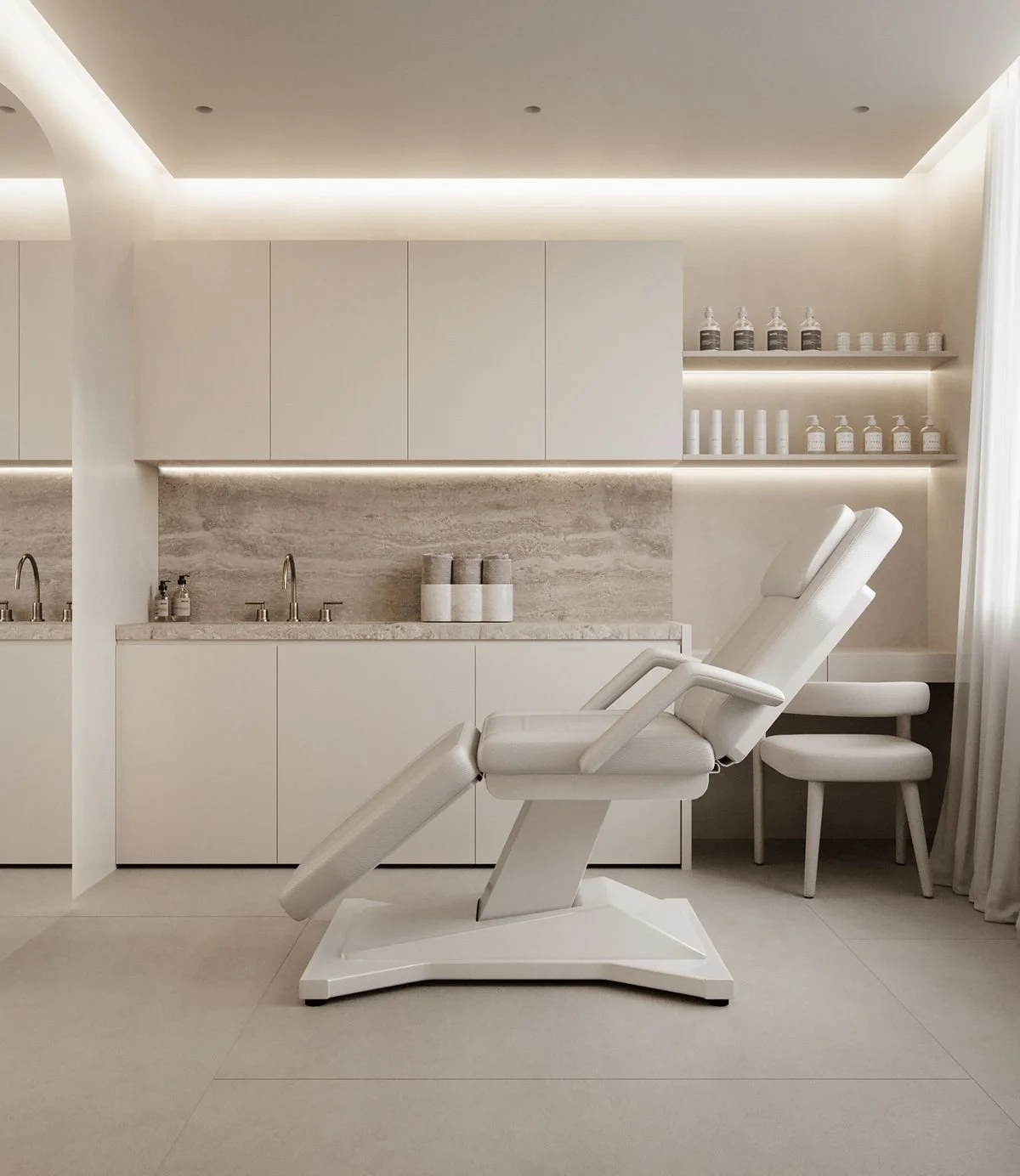 A modern, minimalist medical or spa treatment room with a white reclining chair, cabinetry, and shelves holding bottles, with neutral tones and soft lighting.