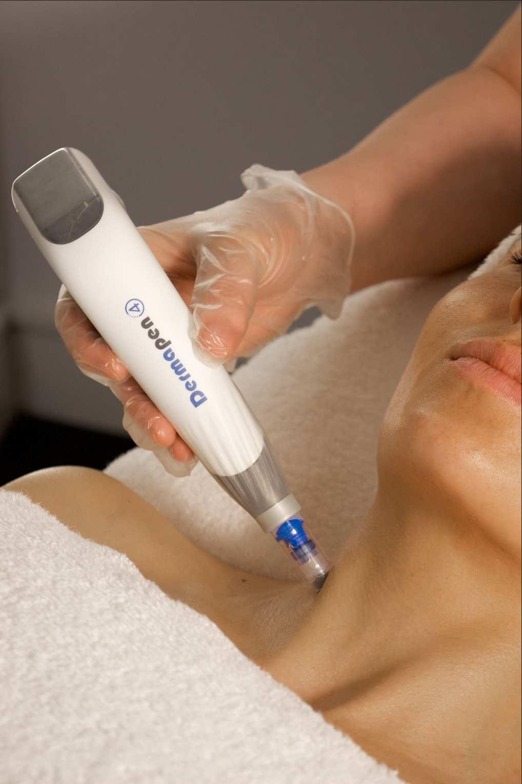 A person receiving a skin treatment with a DermaPen device on their neck during a cosmetic procedure, lying on a white towel.