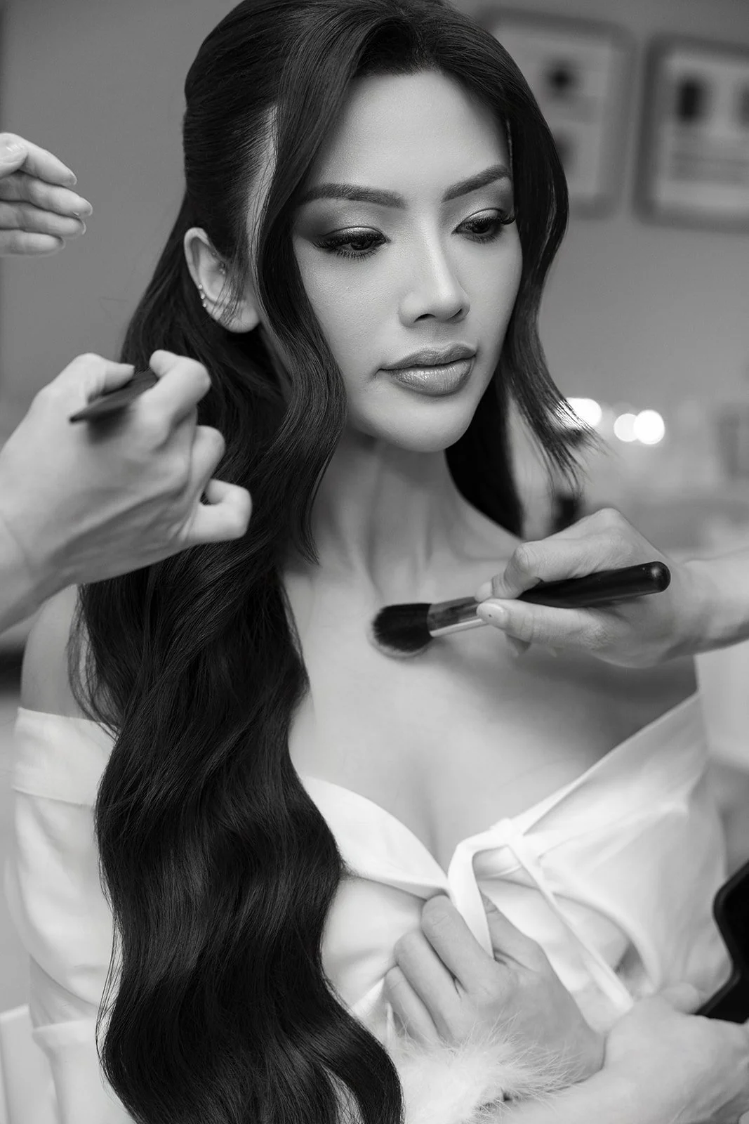 A woman with long wavy hair getting her makeup done by a makeup artist.